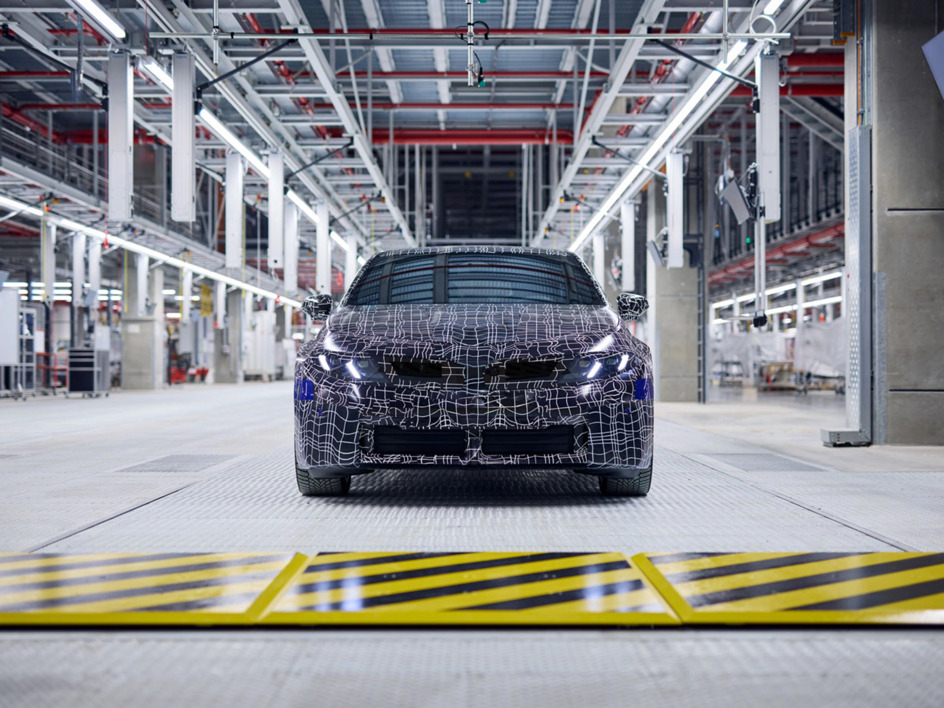 Ein getarntes Auto-Prototyp steht in einer hell beleuchteten Fahrzeugproduktionshalle.