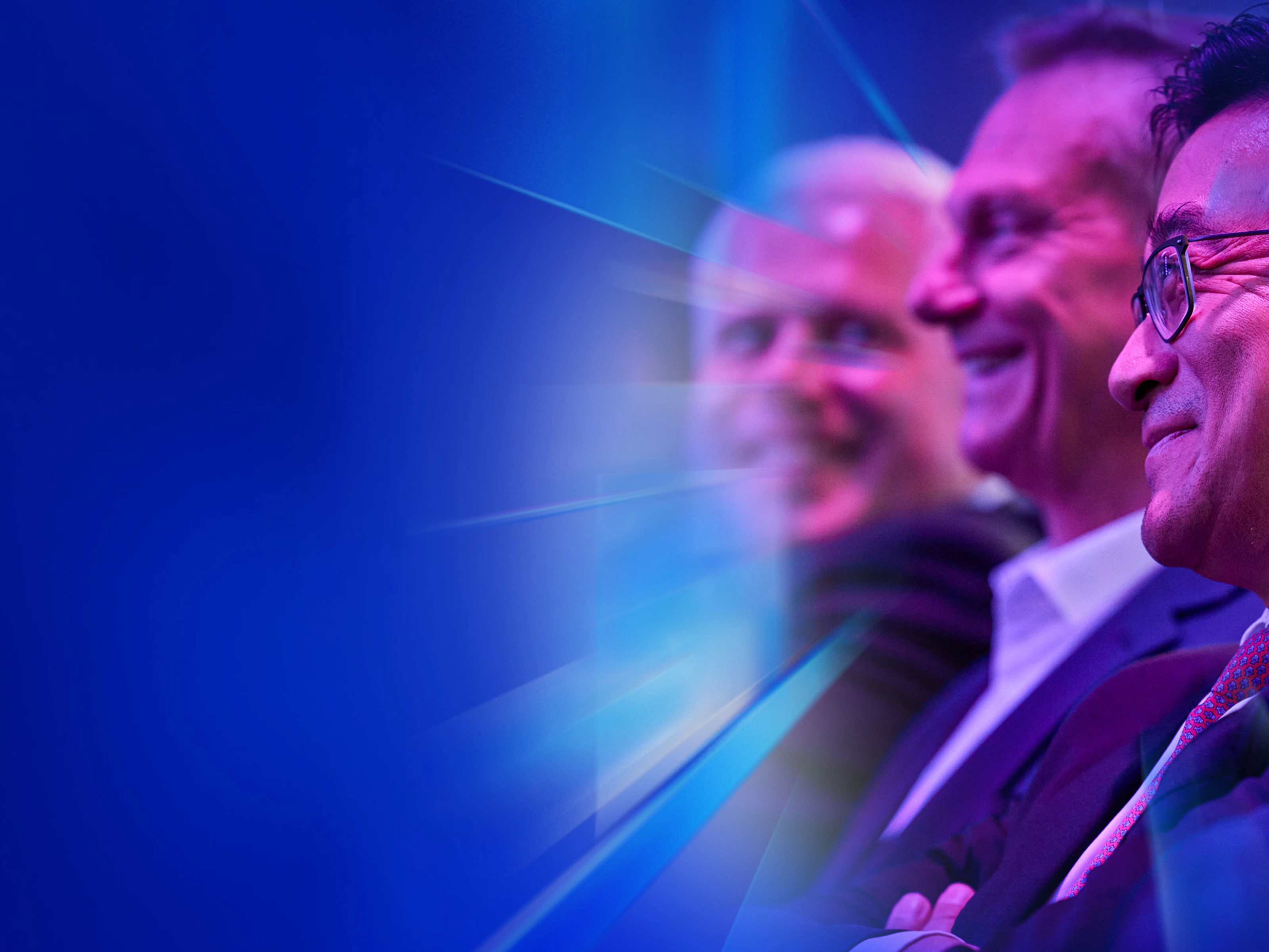 Drei lächelnde Männer im Anzug sitzen beim IAA Summit im Publikum.