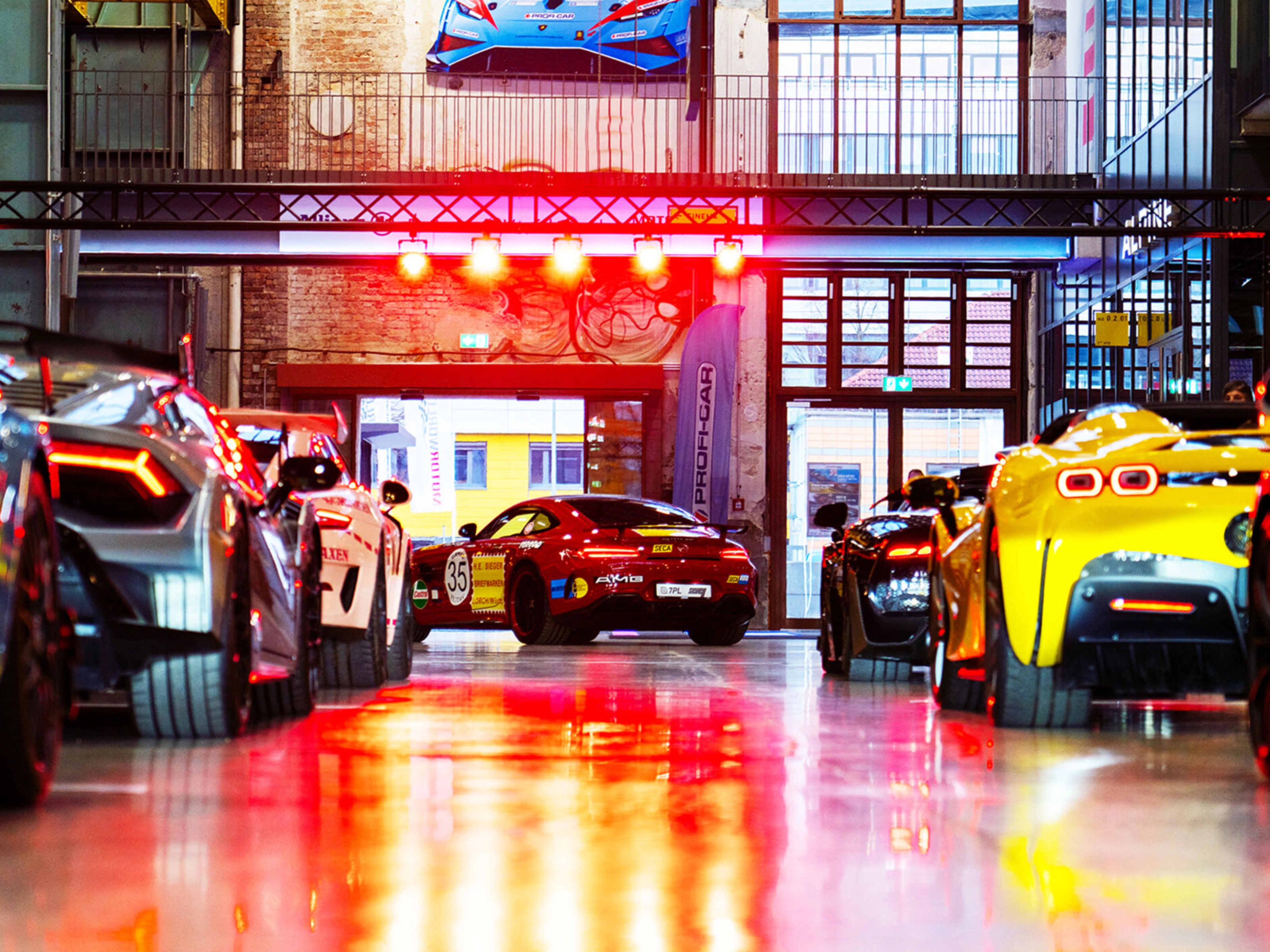 Mehrere Sportwagen stehen in einer hell beleuchteten Industriehalle bei einer Autoausstellung.