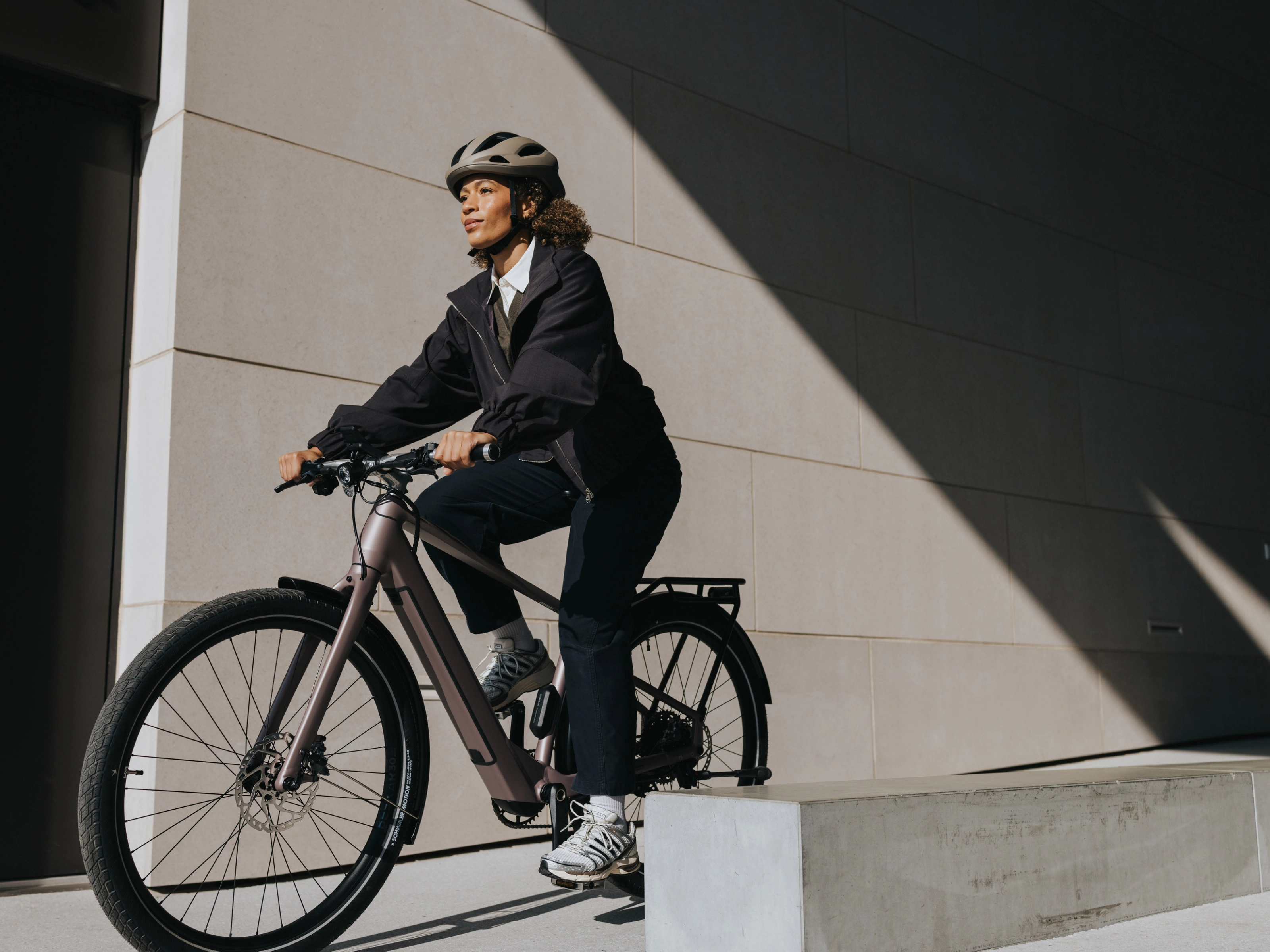 Person mit Helm fährt ein E-Bike neben einem modernen Gebäude.