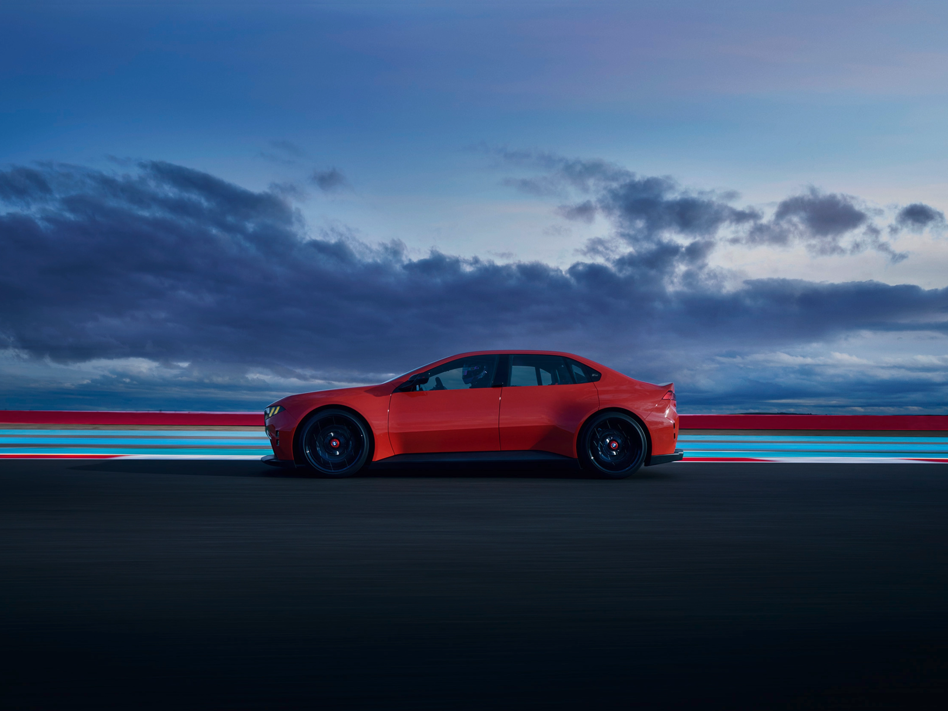 Red car driving on a road at dusk with clouds in the background.