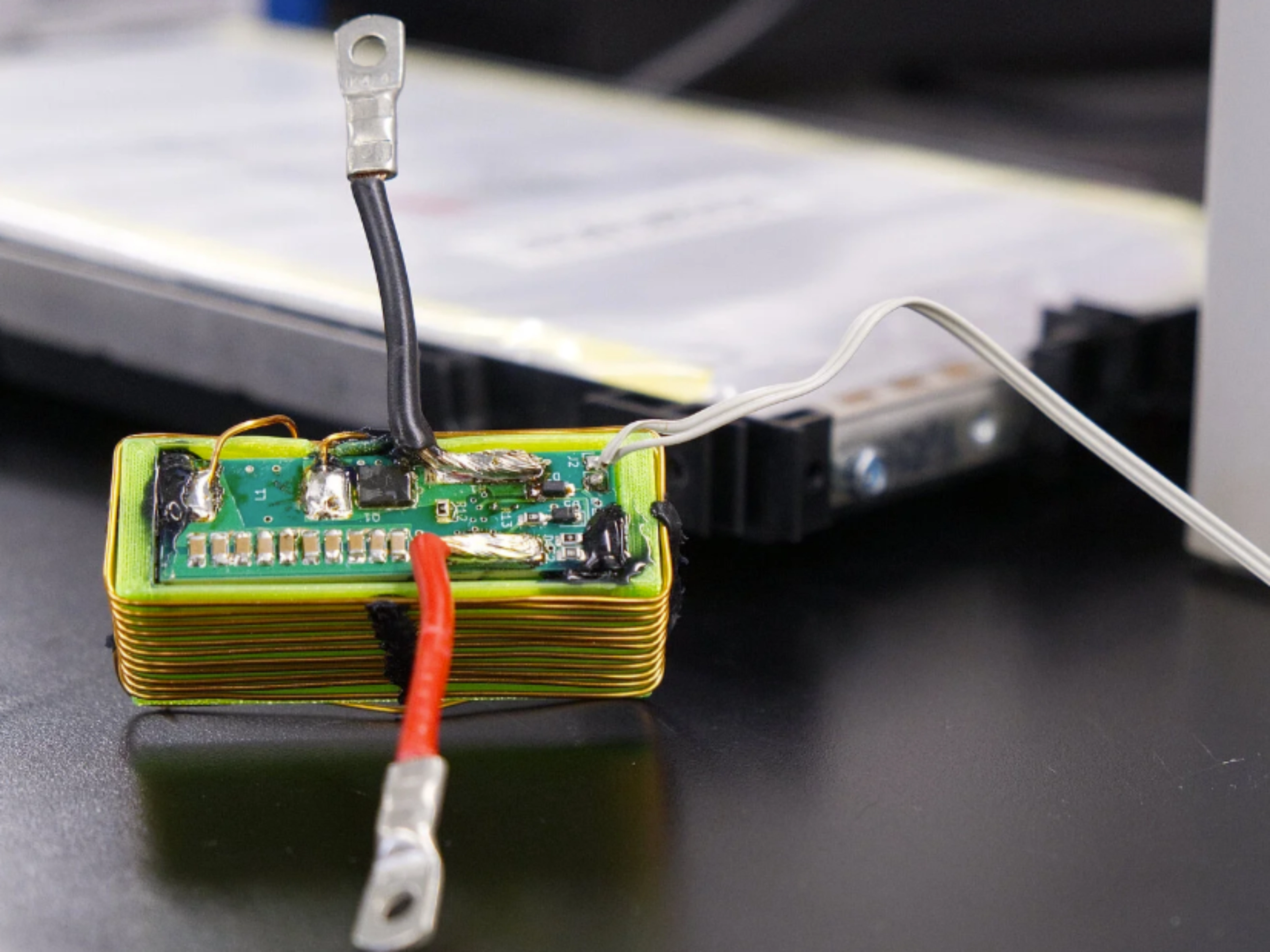 Nahaufnahme eines elektronischen Batteriemoduls mit angeschlossenen Kabeln auf einem Labortisch.