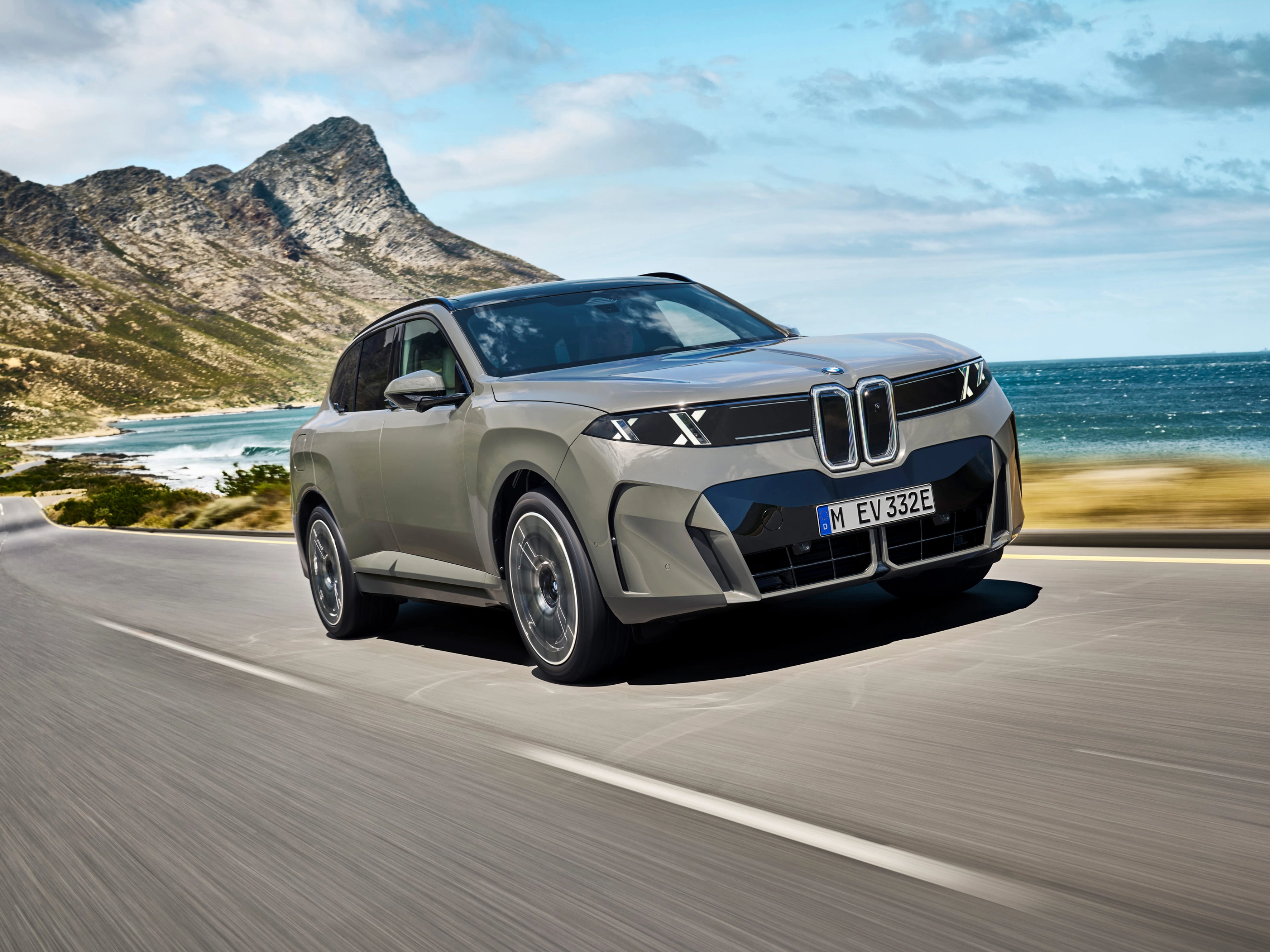 BMW SUV fährt auf einer Küstenstraße mit Bergen und Meer im Hintergrund.
