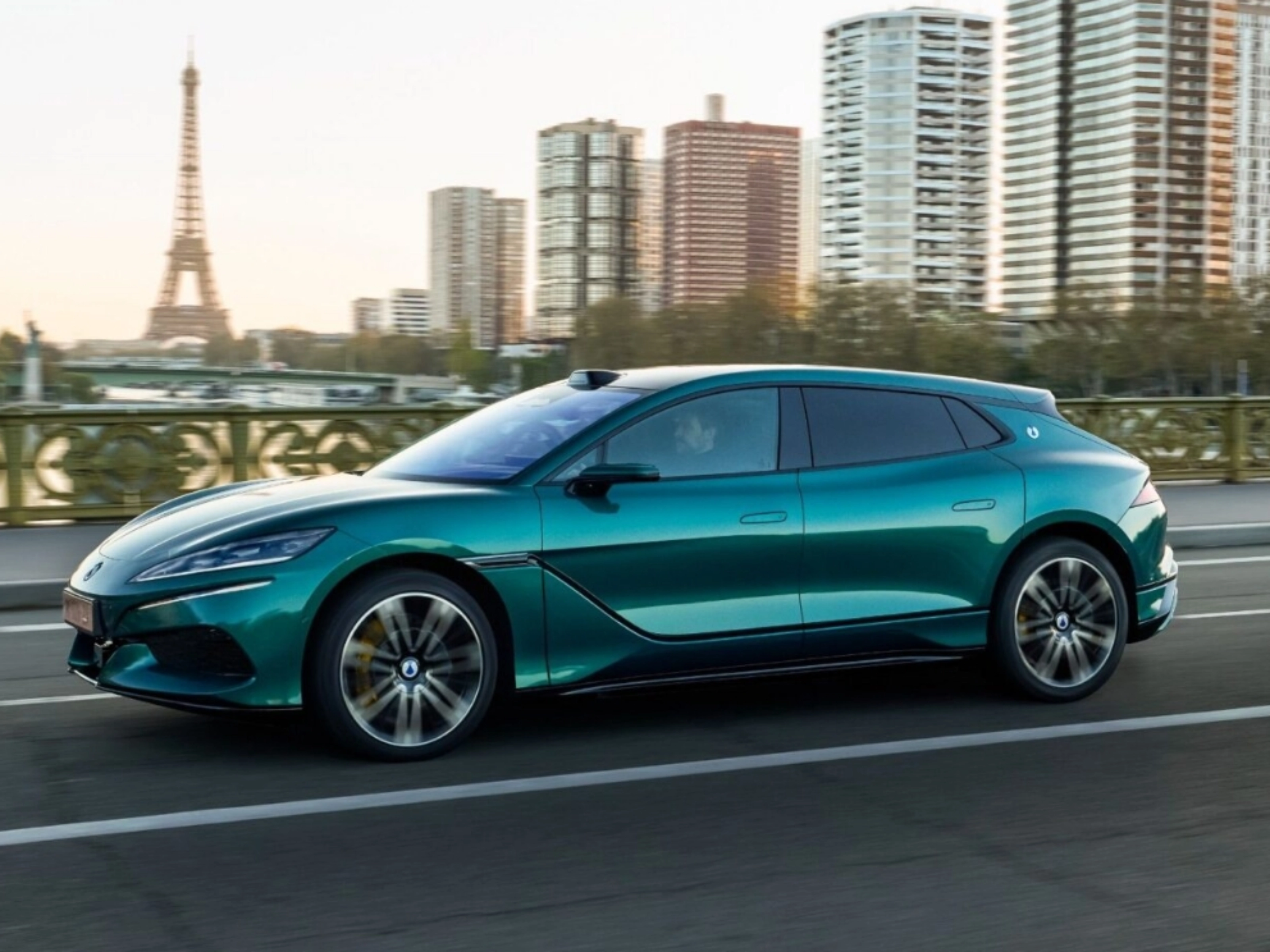 Turquoise BYD electric car driving on a city road with a skyline in the background.