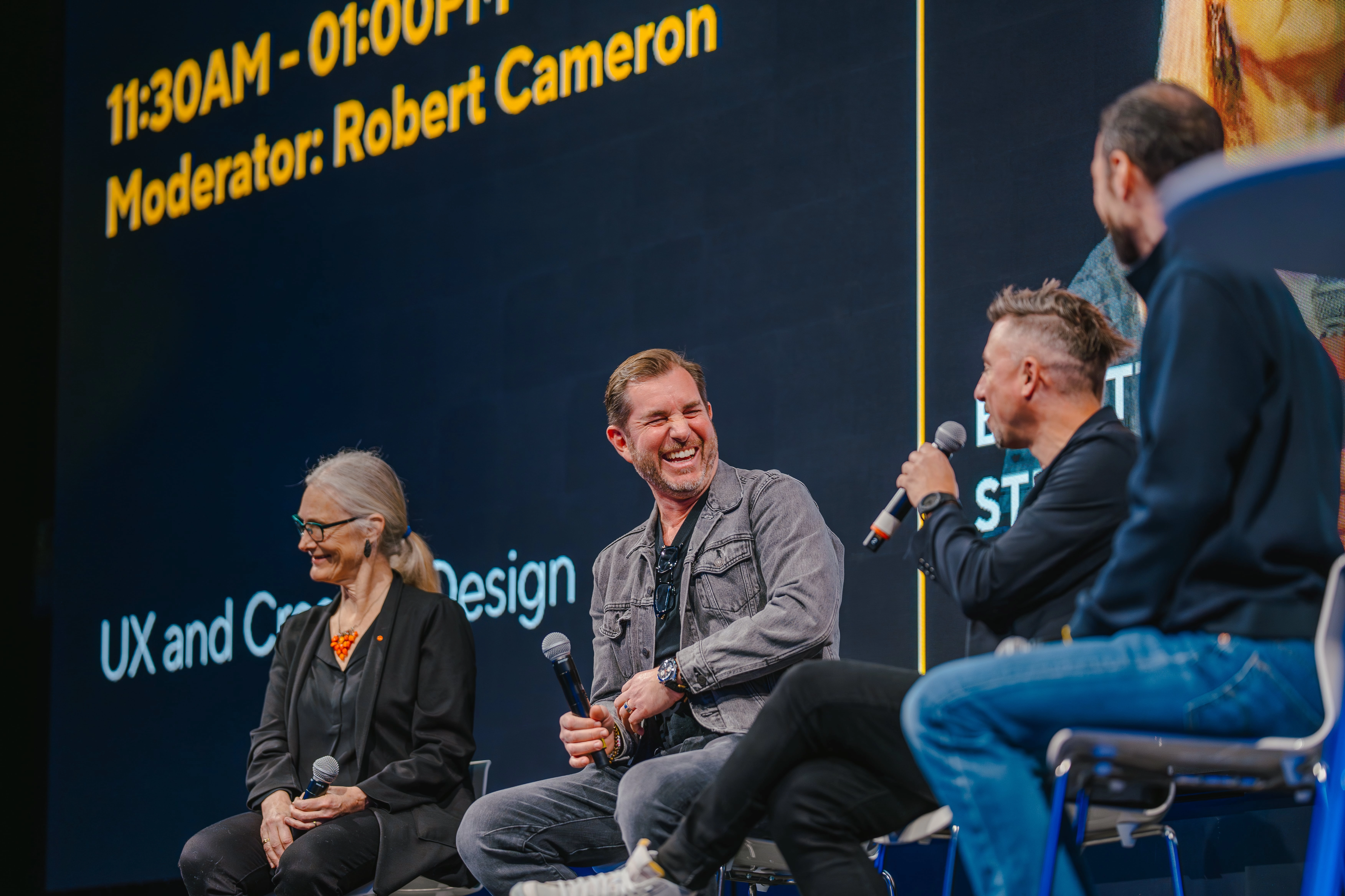 Three people with microphones laugh during a panel discussion on stage.