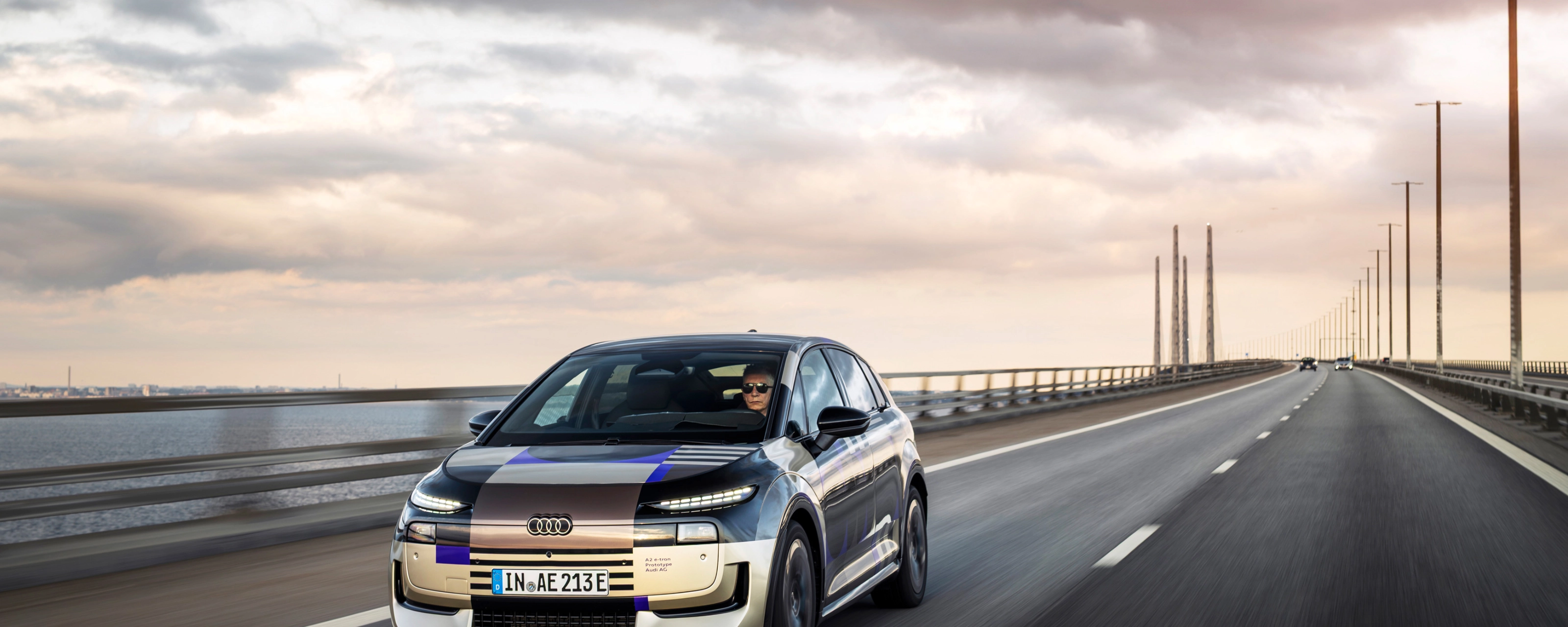 Audi prototype electric vehicle driving on an open road at sunset.