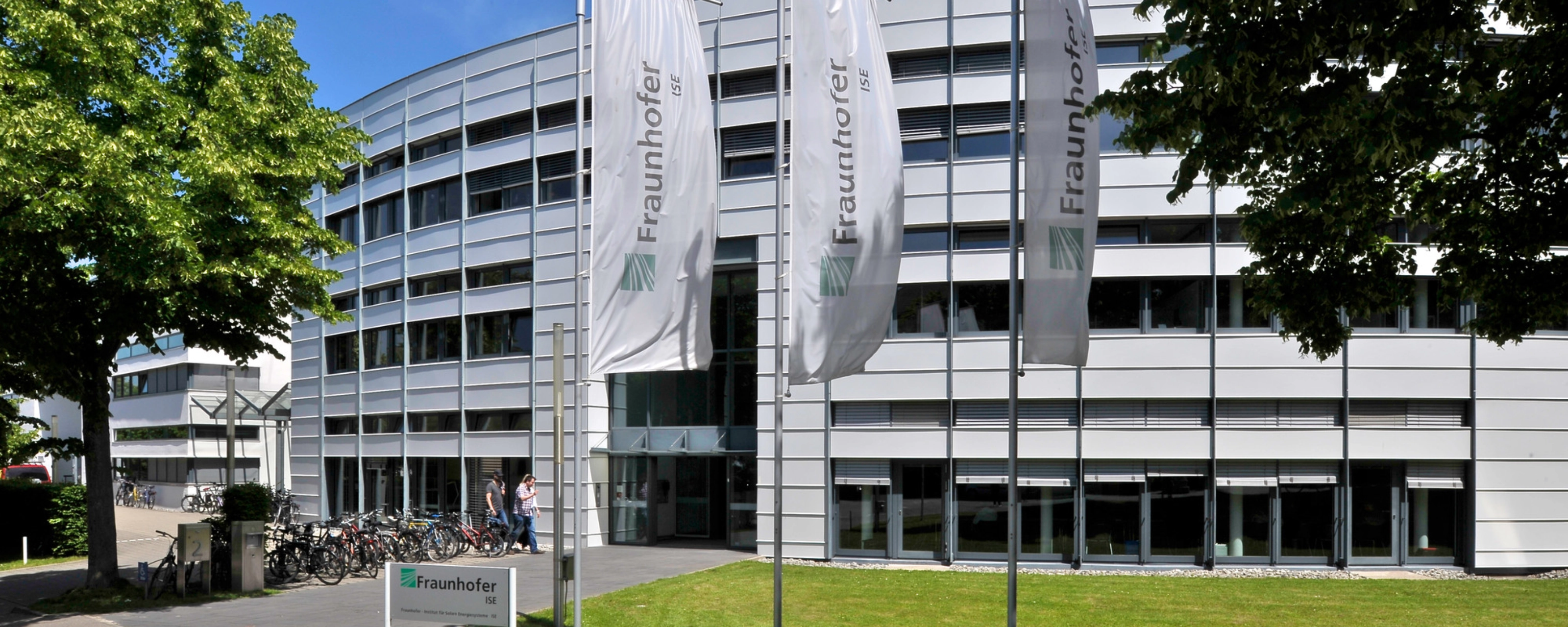Modernes Fraunhofer-Institutsgebäude mit Fahnen und Bäumen davor.