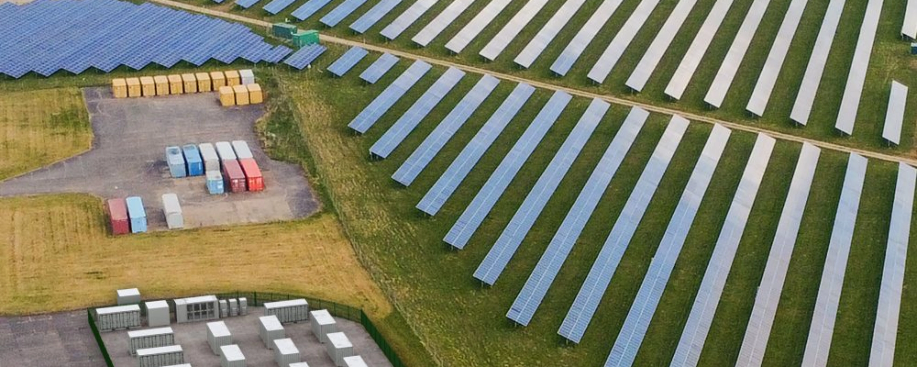 Luftaufnahme einer Solaranlage mit Reihen von Solarpaneelen und mehreren Containern.