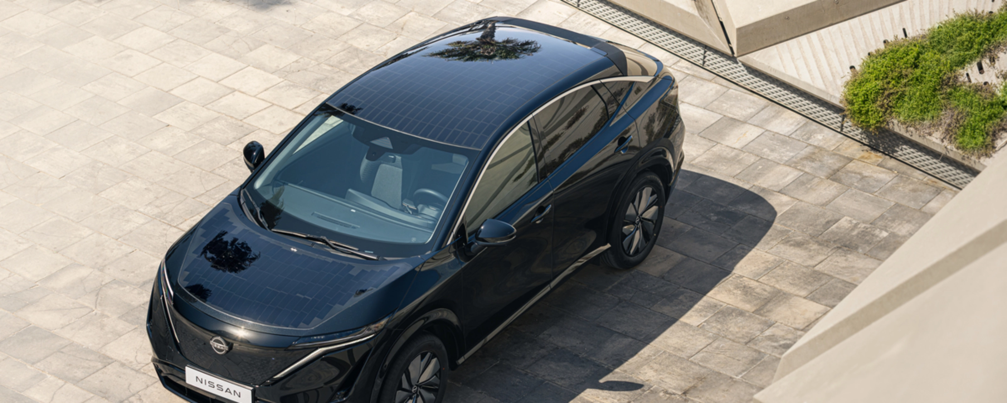 Ein schwarzes Elektro-SUV von Nissan steht auf einer gepflasterten Fläche im Sonnenlicht.