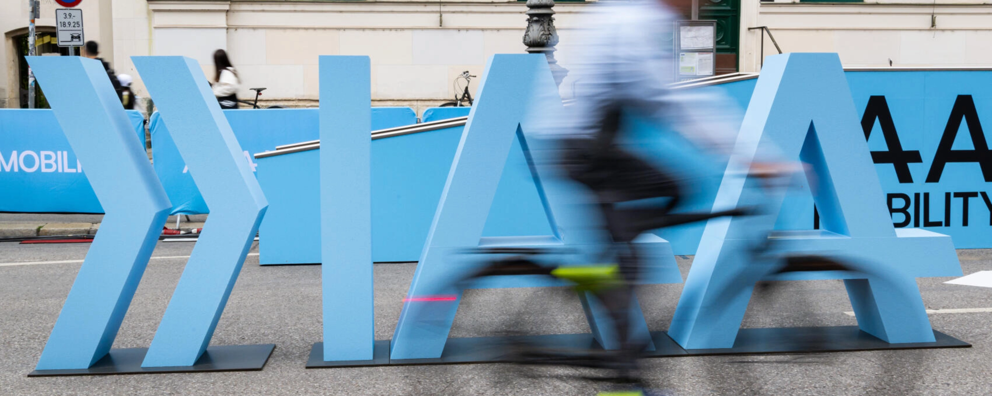 Cyclist rides past large IAA Mobility lettering on a city street.