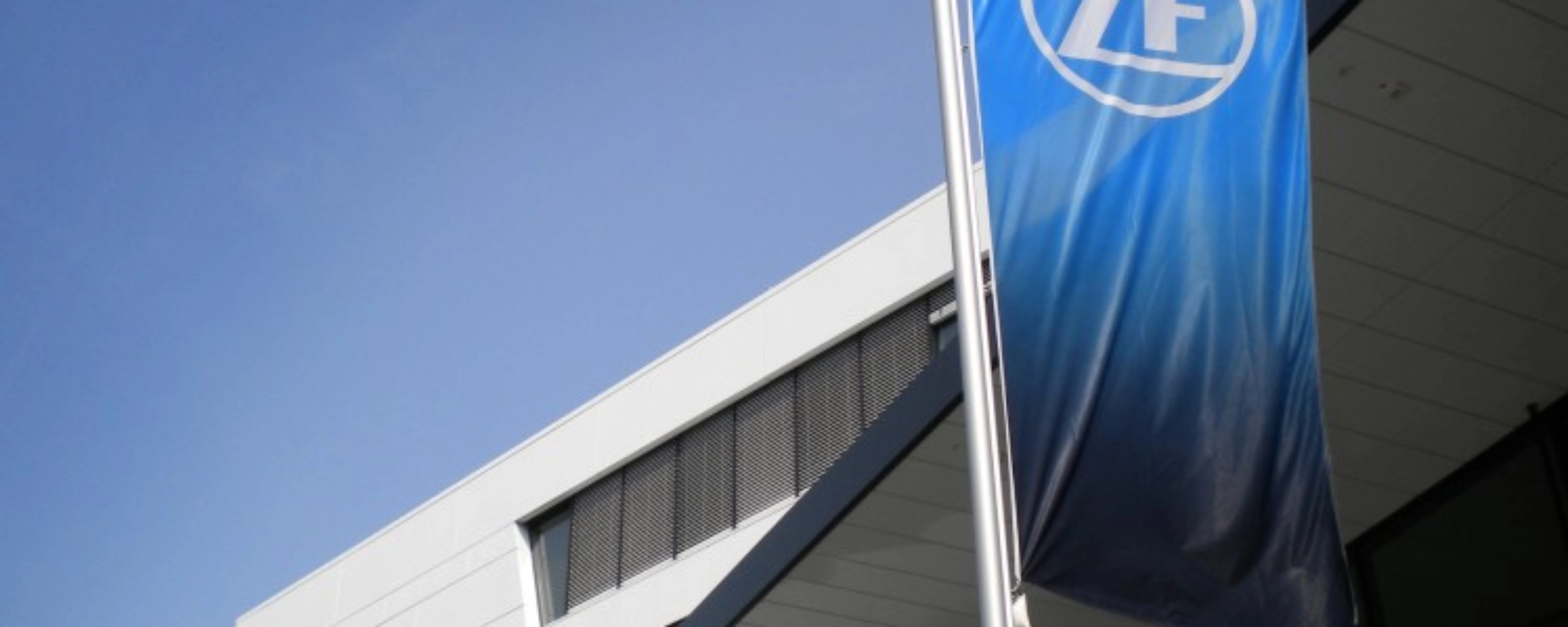 Blaue ZF-Flagge vor einem modernen Bürogebäude mit weißer Fassade.
