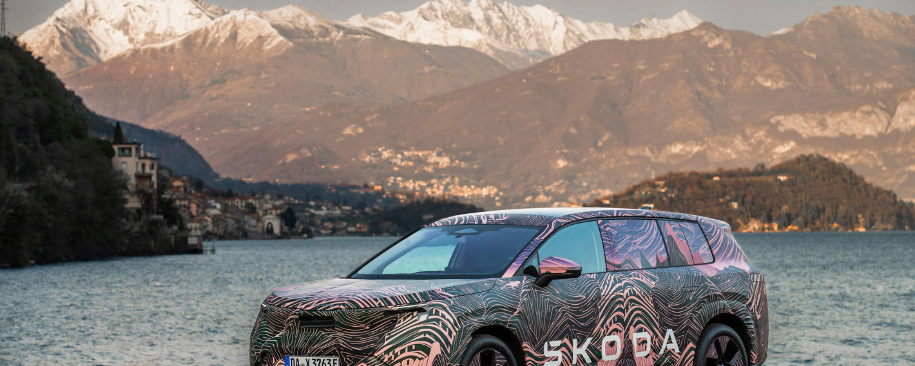 Getarnter Škoda steht am See vor schneebedeckten Bergen.