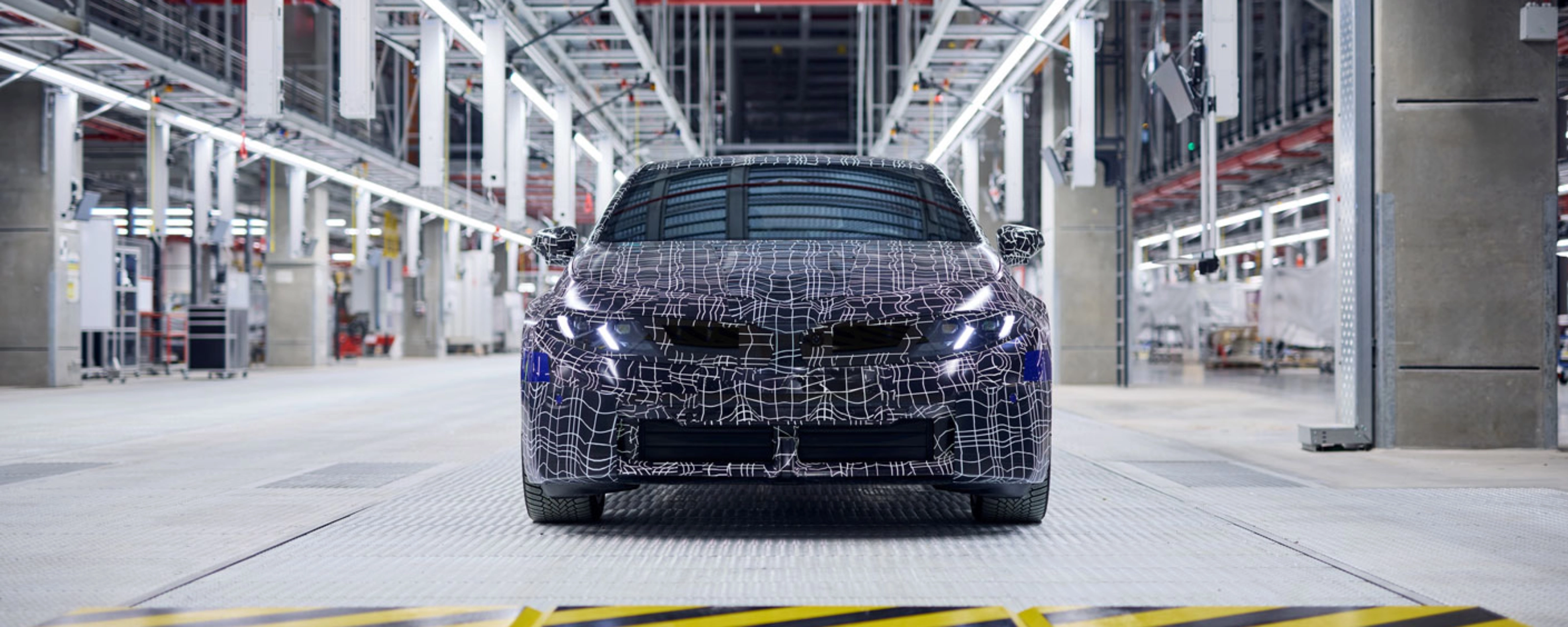 Ein getarntes Auto-Prototyp steht in einer hell beleuchteten Fahrzeugproduktionshalle.