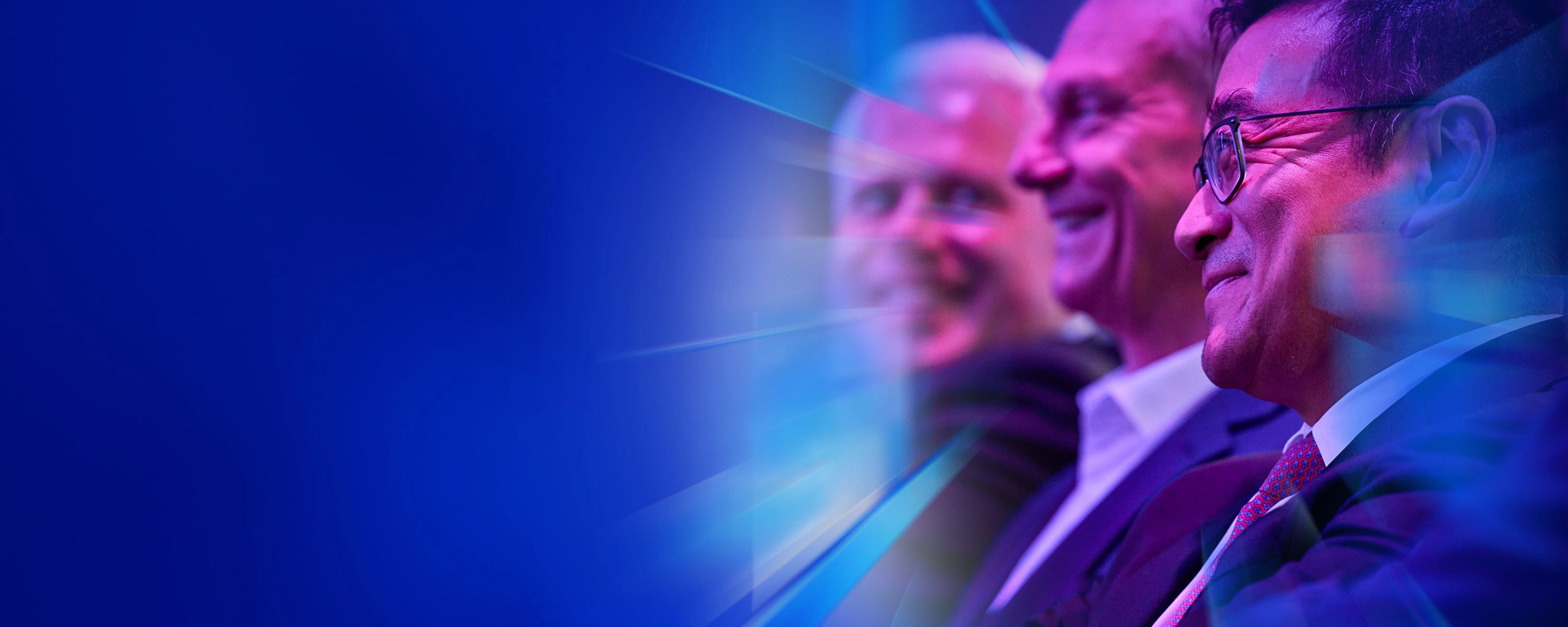 Drei lächelnde Männer im Anzug sitzen beim IAA Summit im Publikum.