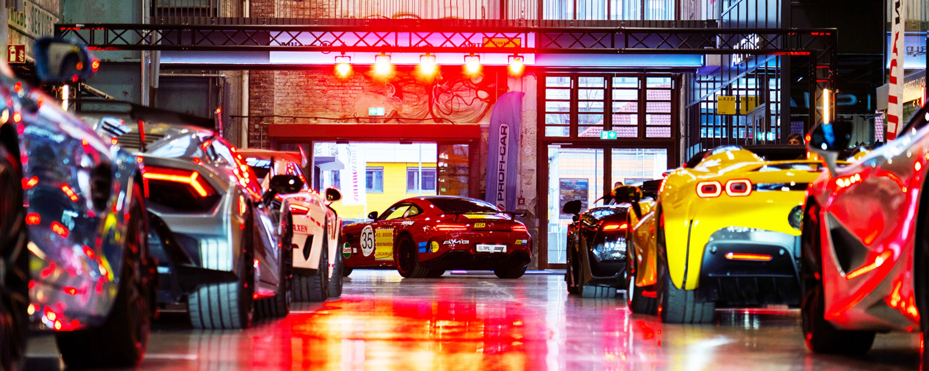 Mehrere Sportwagen stehen in einer hell beleuchteten Industriehalle bei einer Autoausstellung.