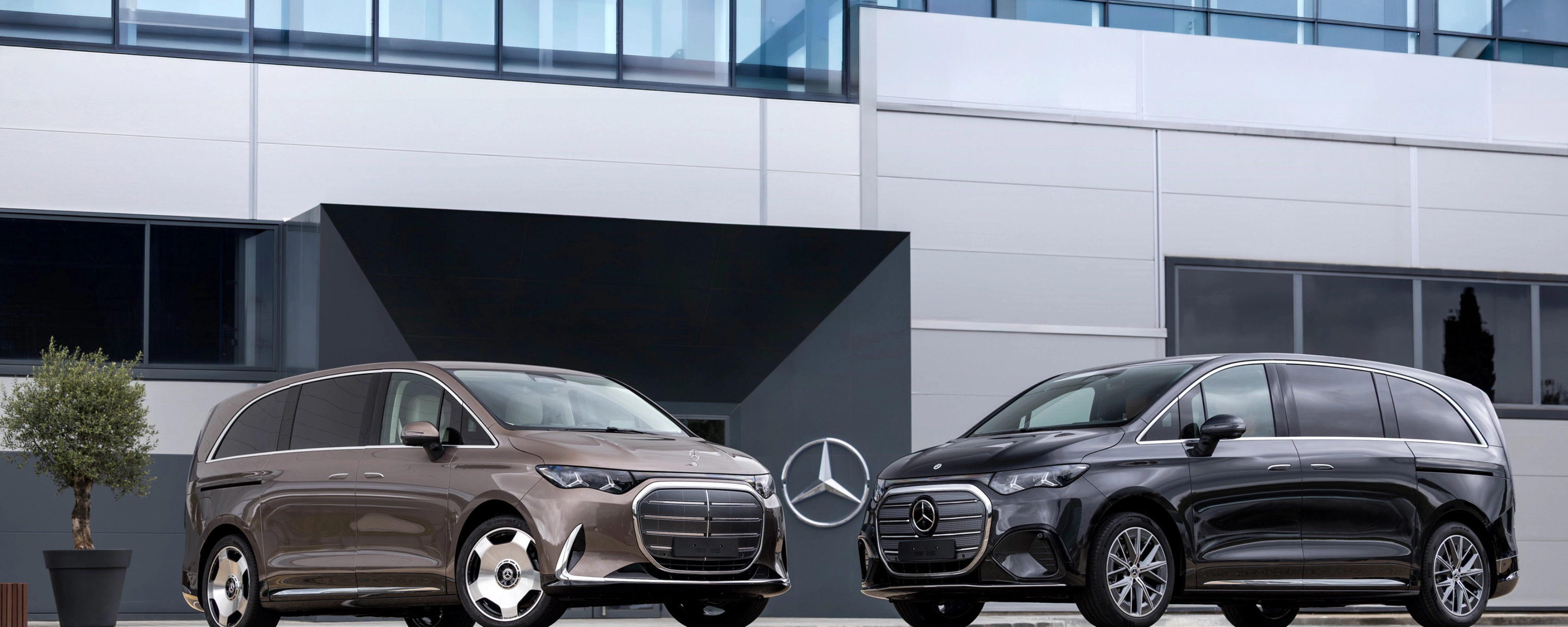 Two Mercedes-Benz vans parked in front of a modern office building.