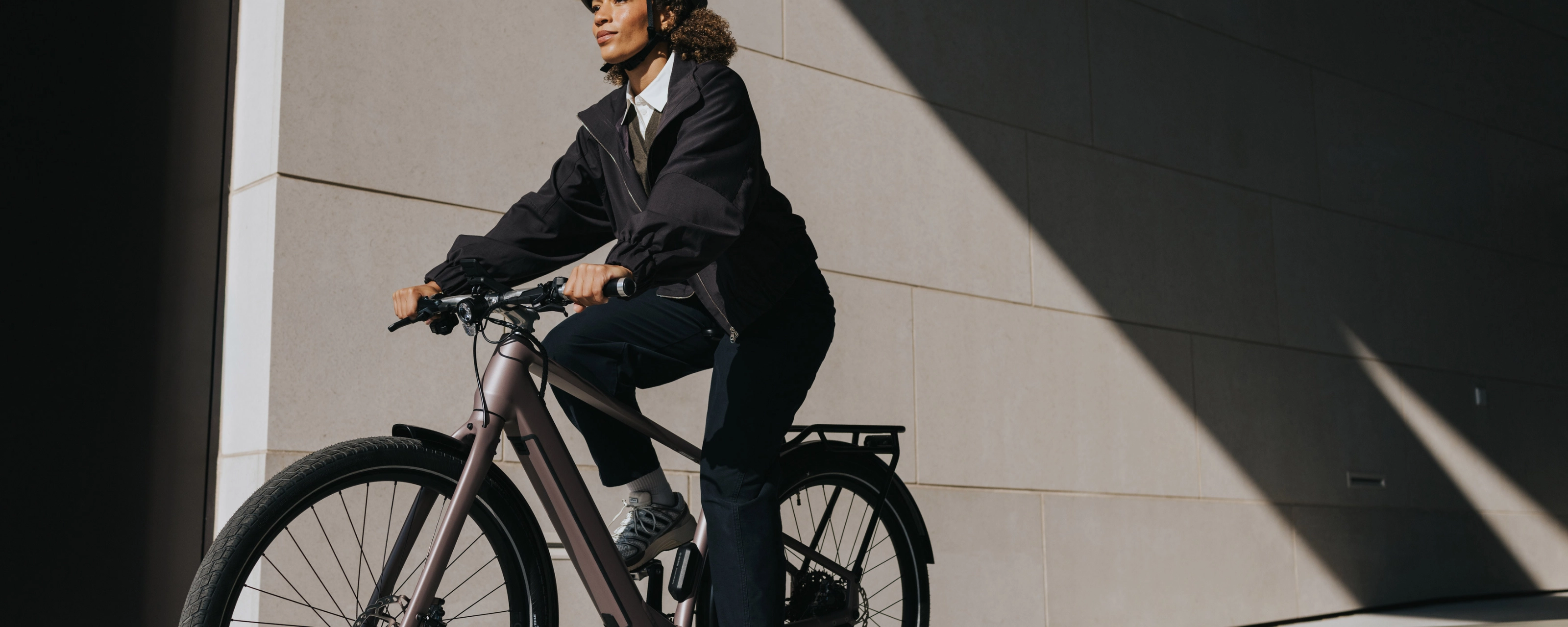 Person mit Helm fährt ein E-Bike neben einem modernen Gebäude.
