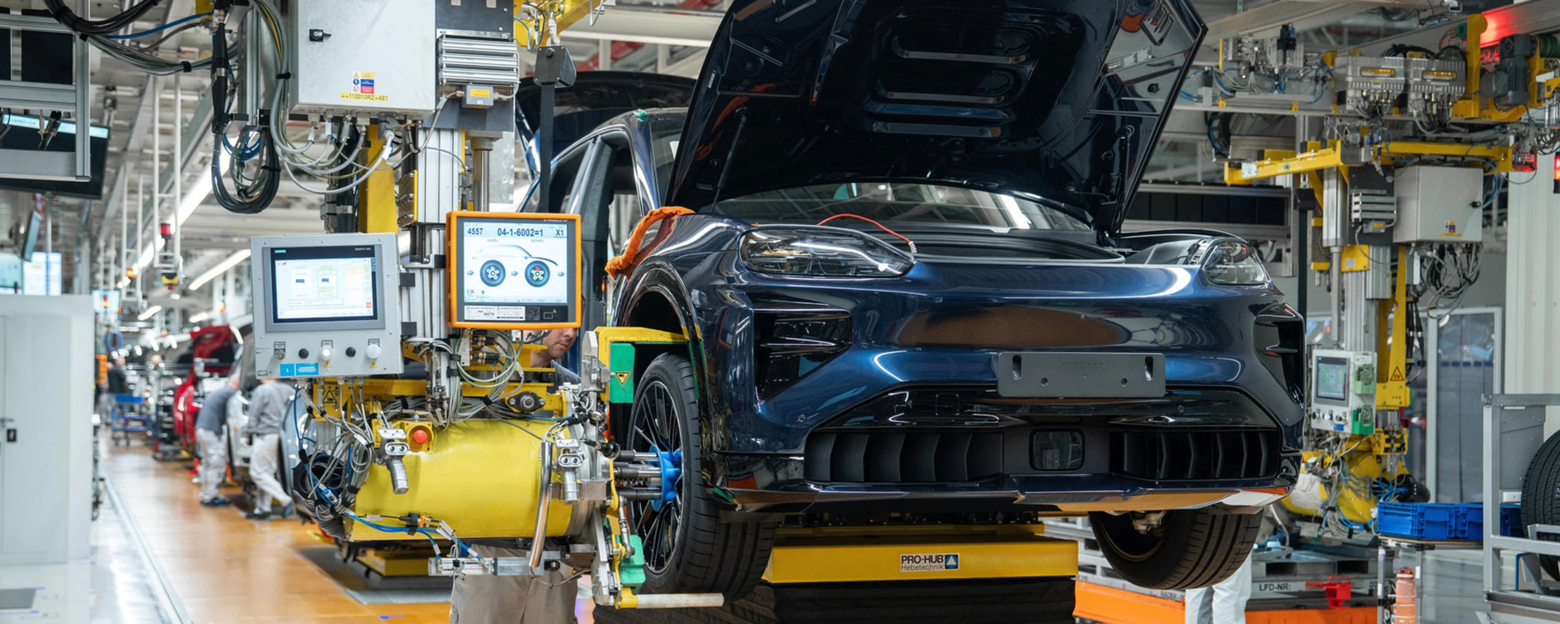 Teilmontiertes Elektroauto auf dem Montageband mit offenem Kofferraum und Maschinen ringsum.