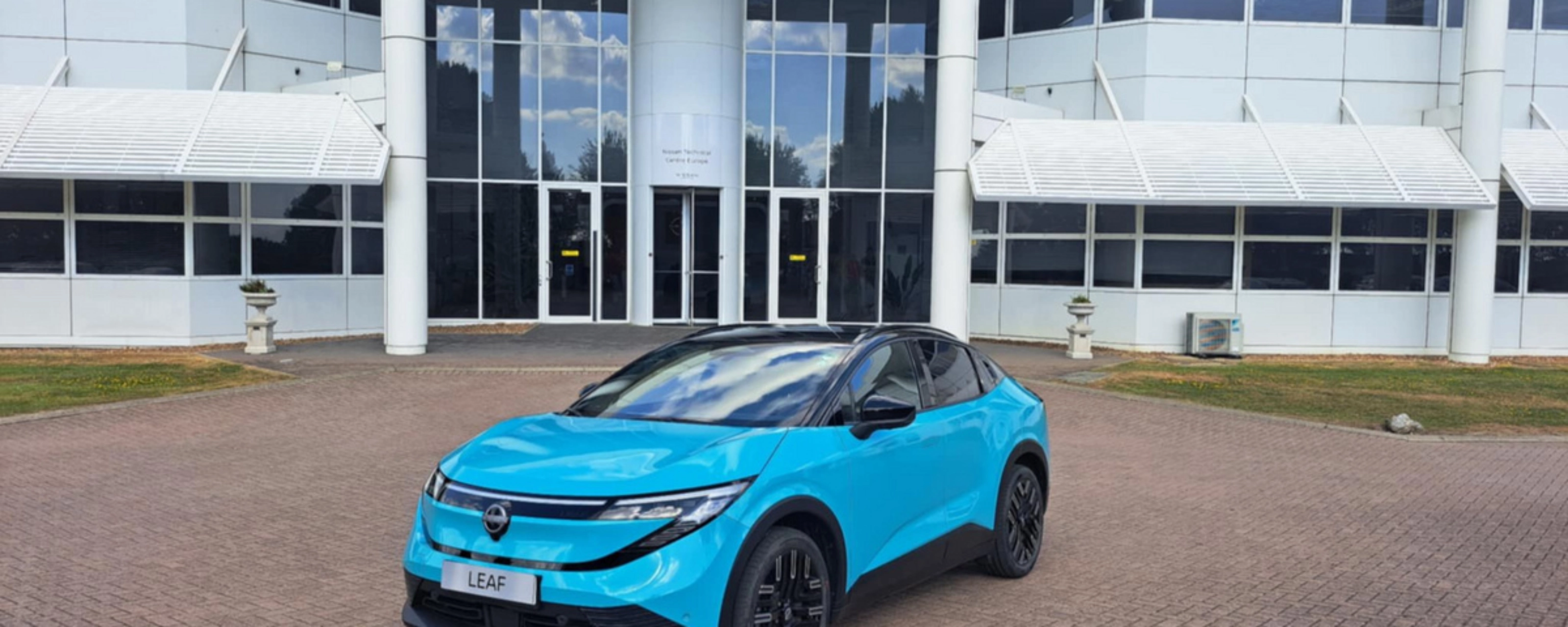 Blauer Nissan Crossover steht vor einem modernen Gebäude mit Glasfassade.