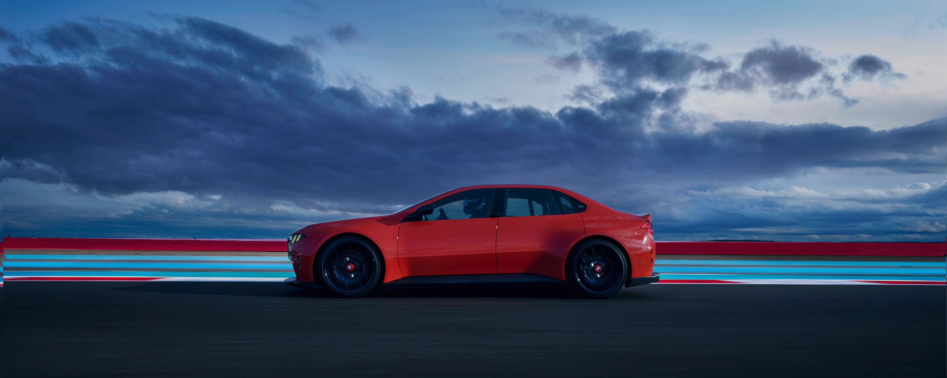 Red car driving on a road at dusk with clouds in the background.