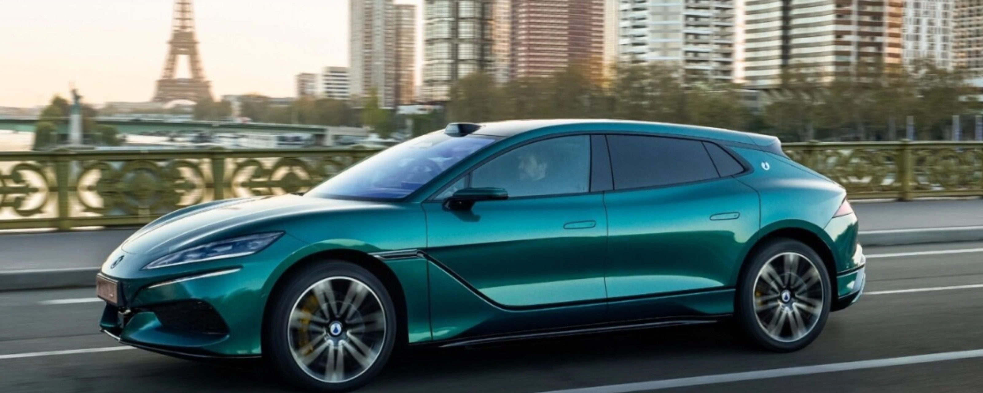 Turquoise BYD electric car driving on a city road with a skyline in the background.