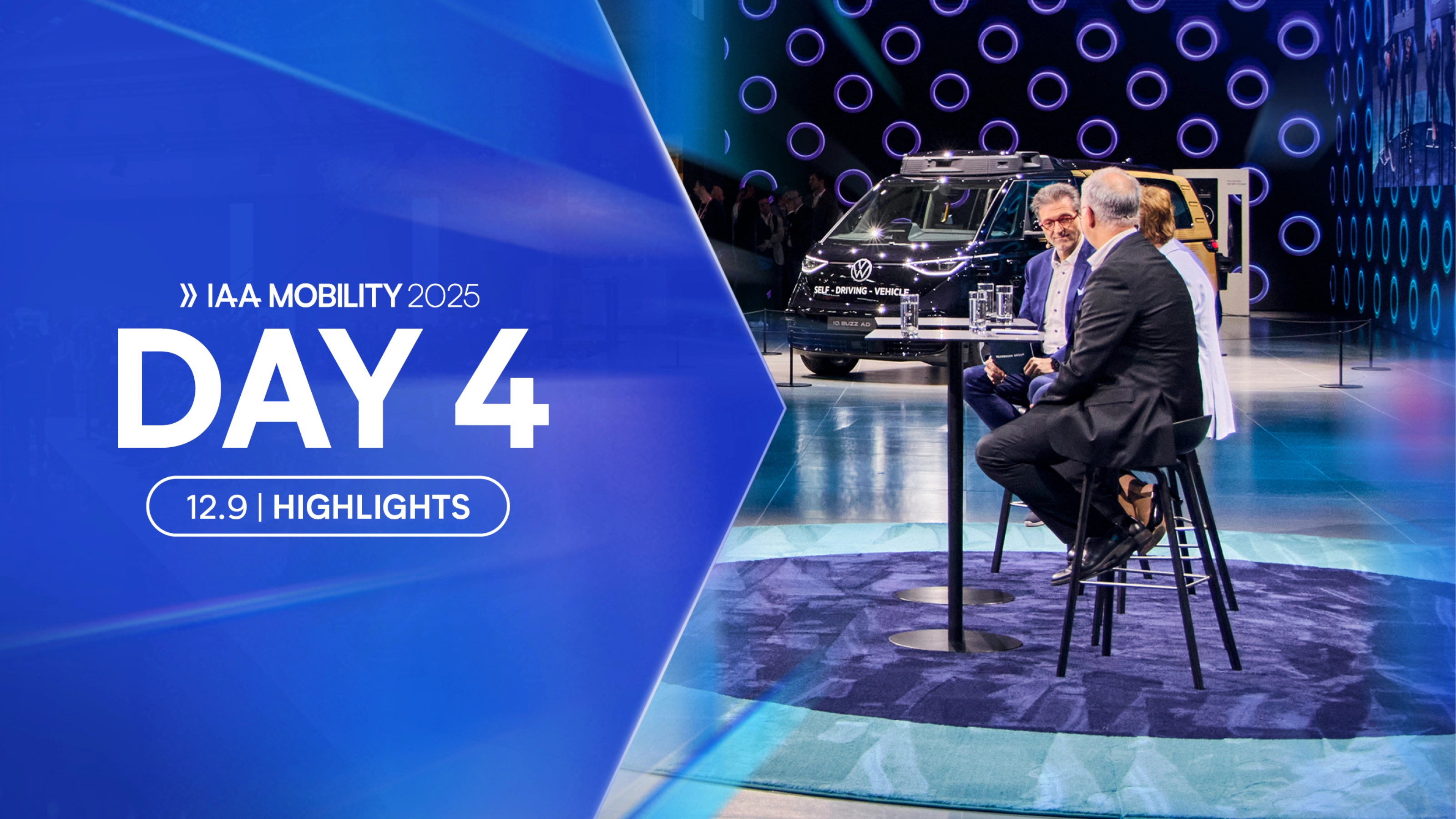 Three people talk on stage at IAA Mobility 2025 with a self-driving VW van in the background.