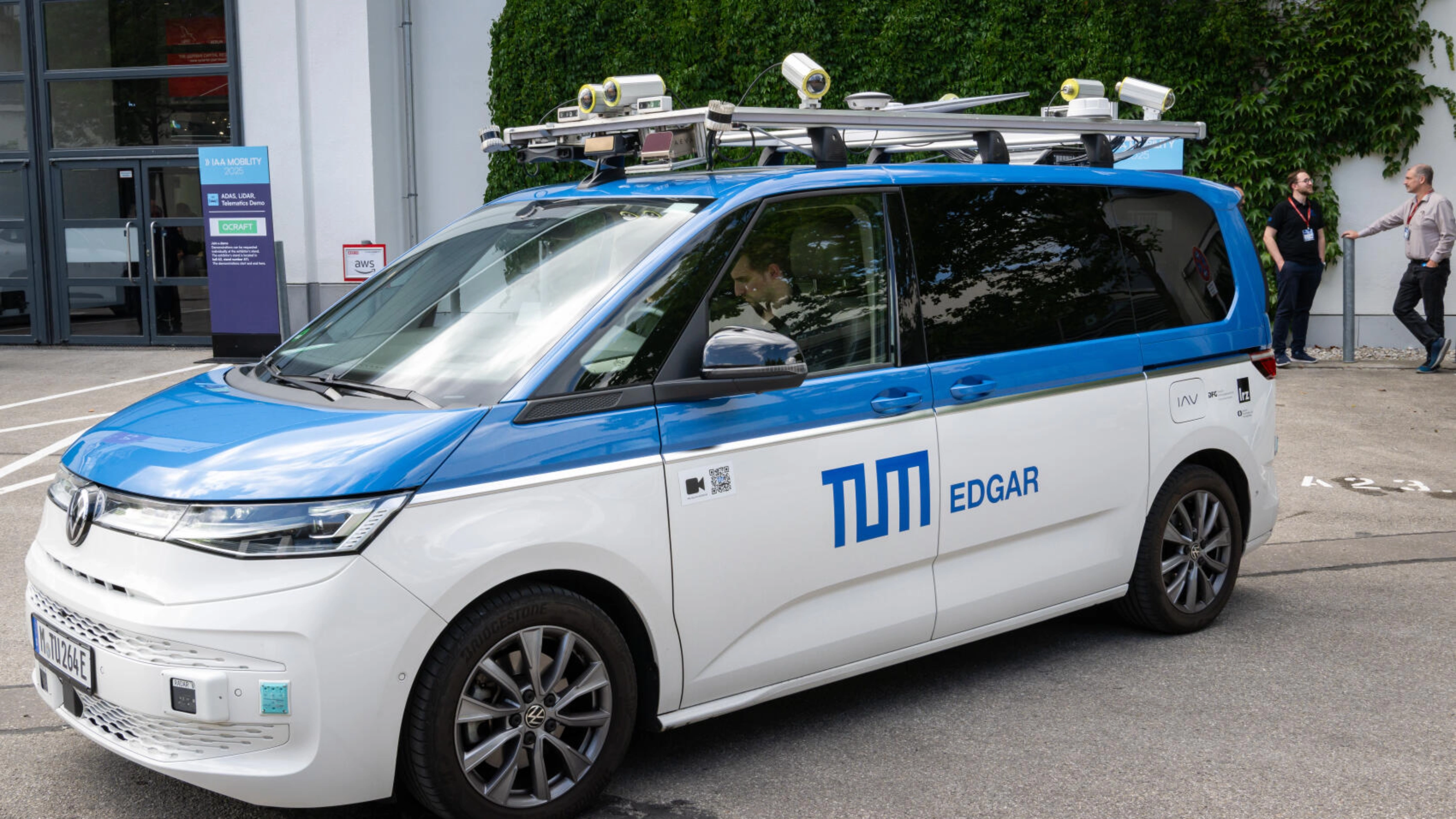 Testfahrzeug mit Sensoren auf dem Dach steht auf einem Eventgelände.