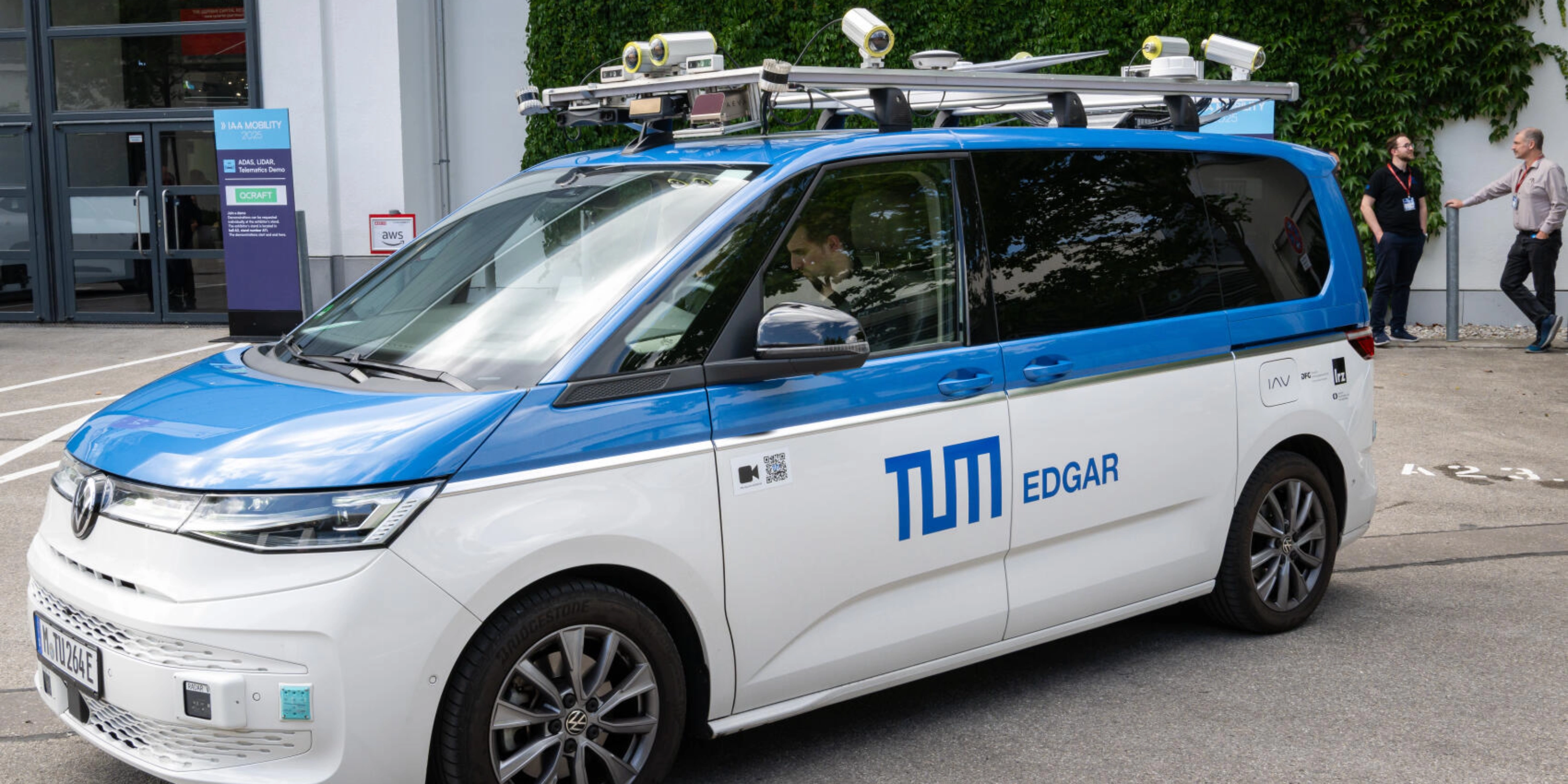 Testfahrzeug mit Sensoren auf dem Dach steht auf einem Eventgelände.