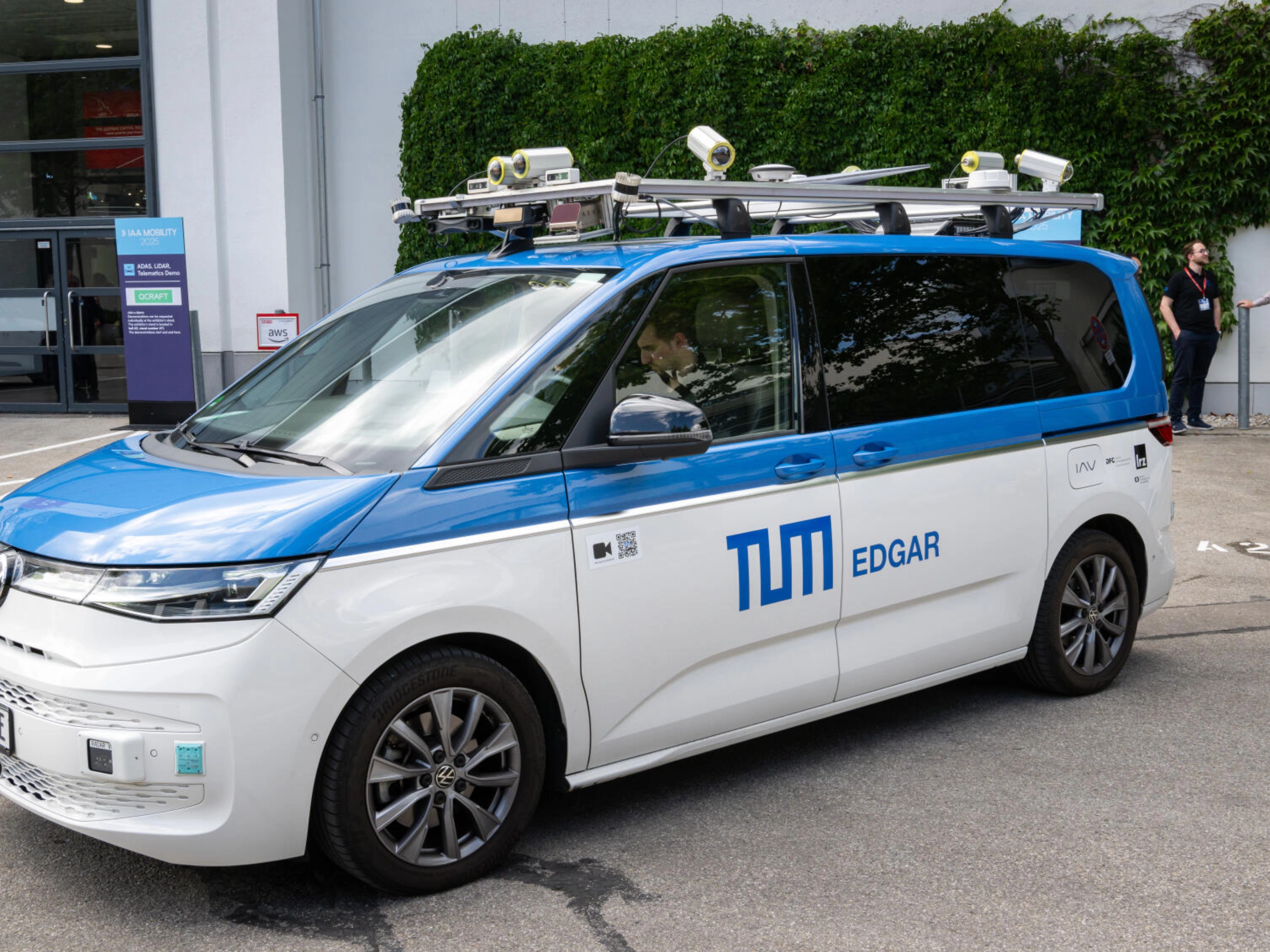 Testfahrzeug mit Sensoren auf dem Dach steht auf einem Eventgelände.