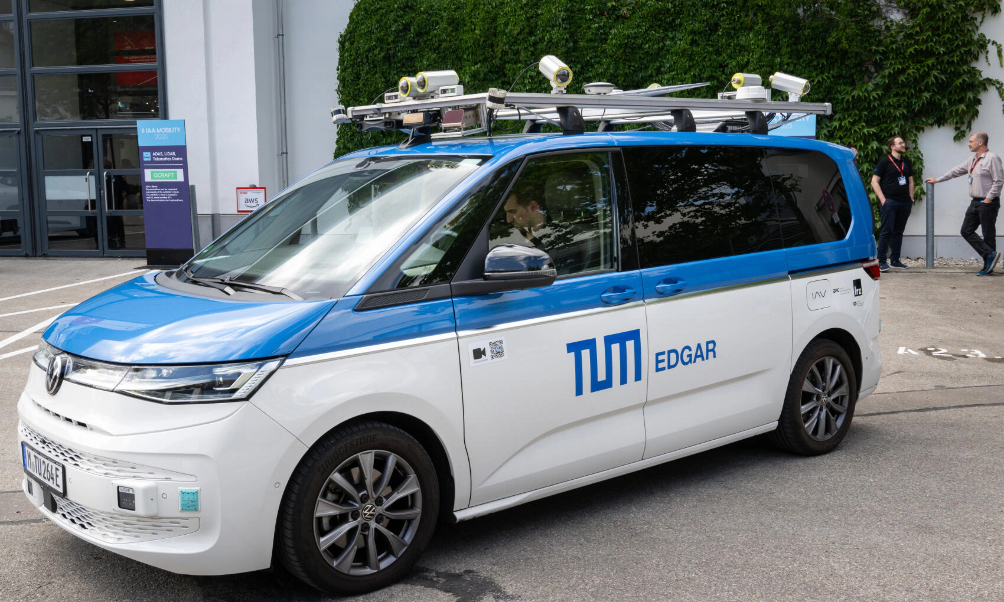 Testfahrzeug mit Sensoren auf dem Dach steht auf einem Eventgelände.
