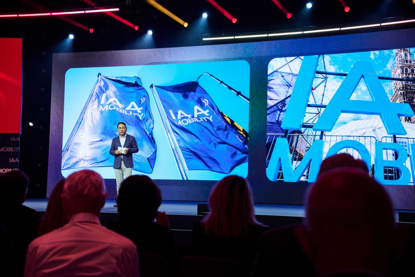 A speaker presents on stage at the IAA Mobility event in front of large branded visuals.
