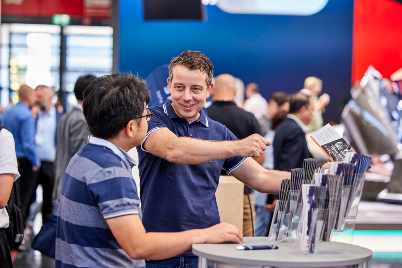 Zwei Männer im Gespräch an einem Stand mit Broschüren auf der IAA MOBILITY 2023.