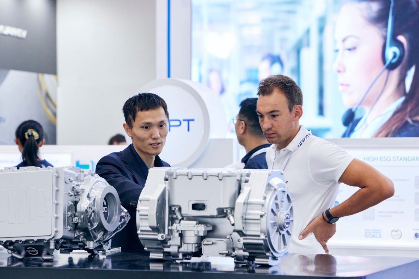 Two men examine electric drive components on display at a mobility trade fair booth.
