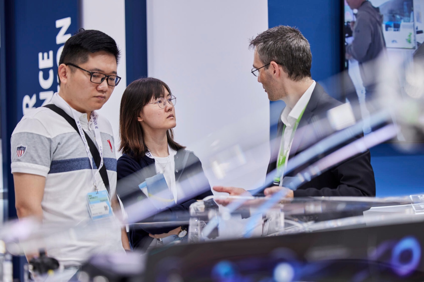 Drei Personen sprechen auf einem Mobilitäts-Messestand über technische Details mit transparenten Bauteilen.