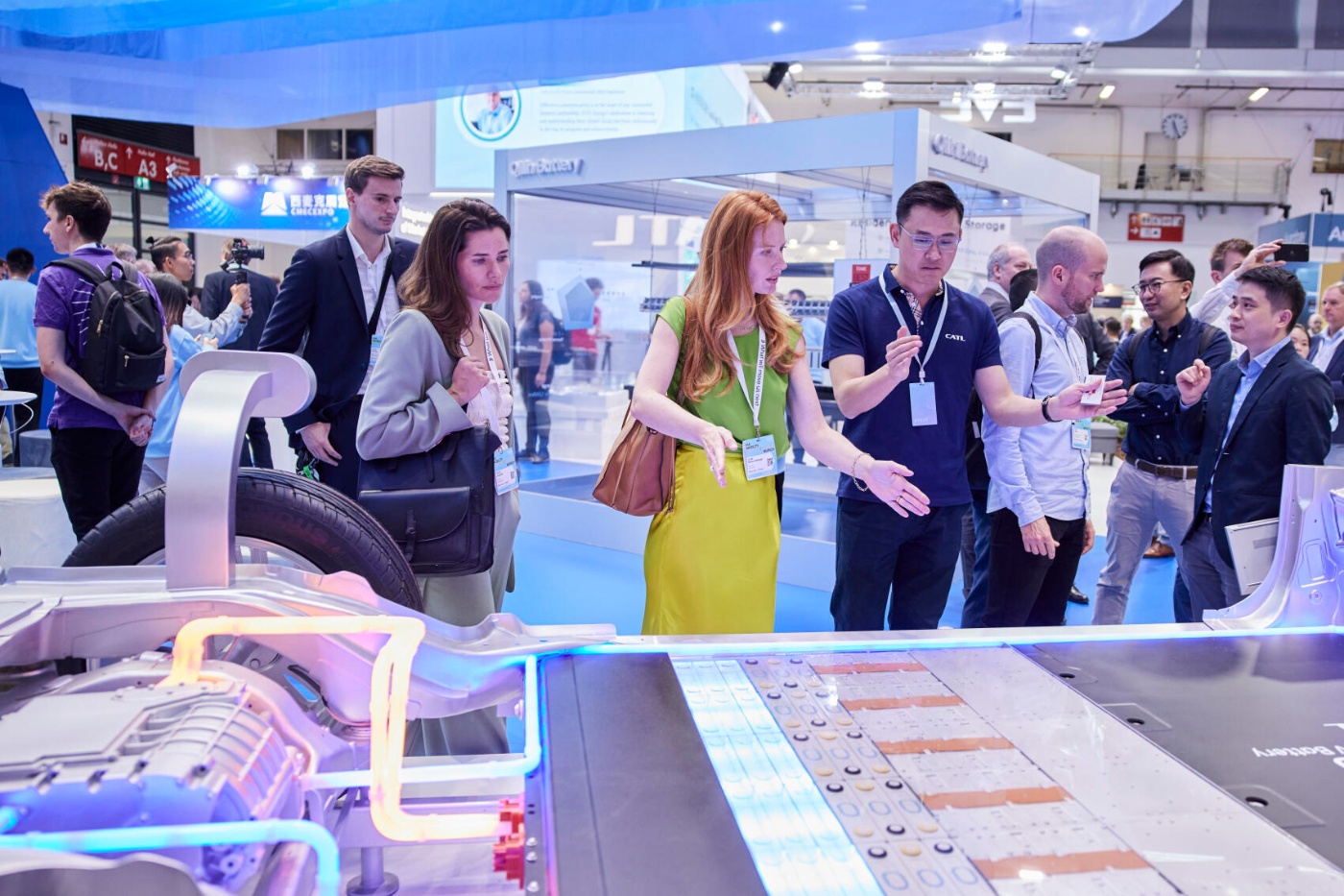 Group of people discussing an illuminated electric vehicle battery system at a trade show booth.