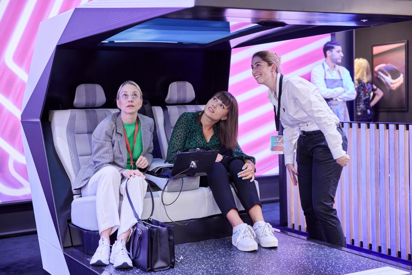Three women explore a futuristic vehicle interior display with ambient lighting at a trade fair.