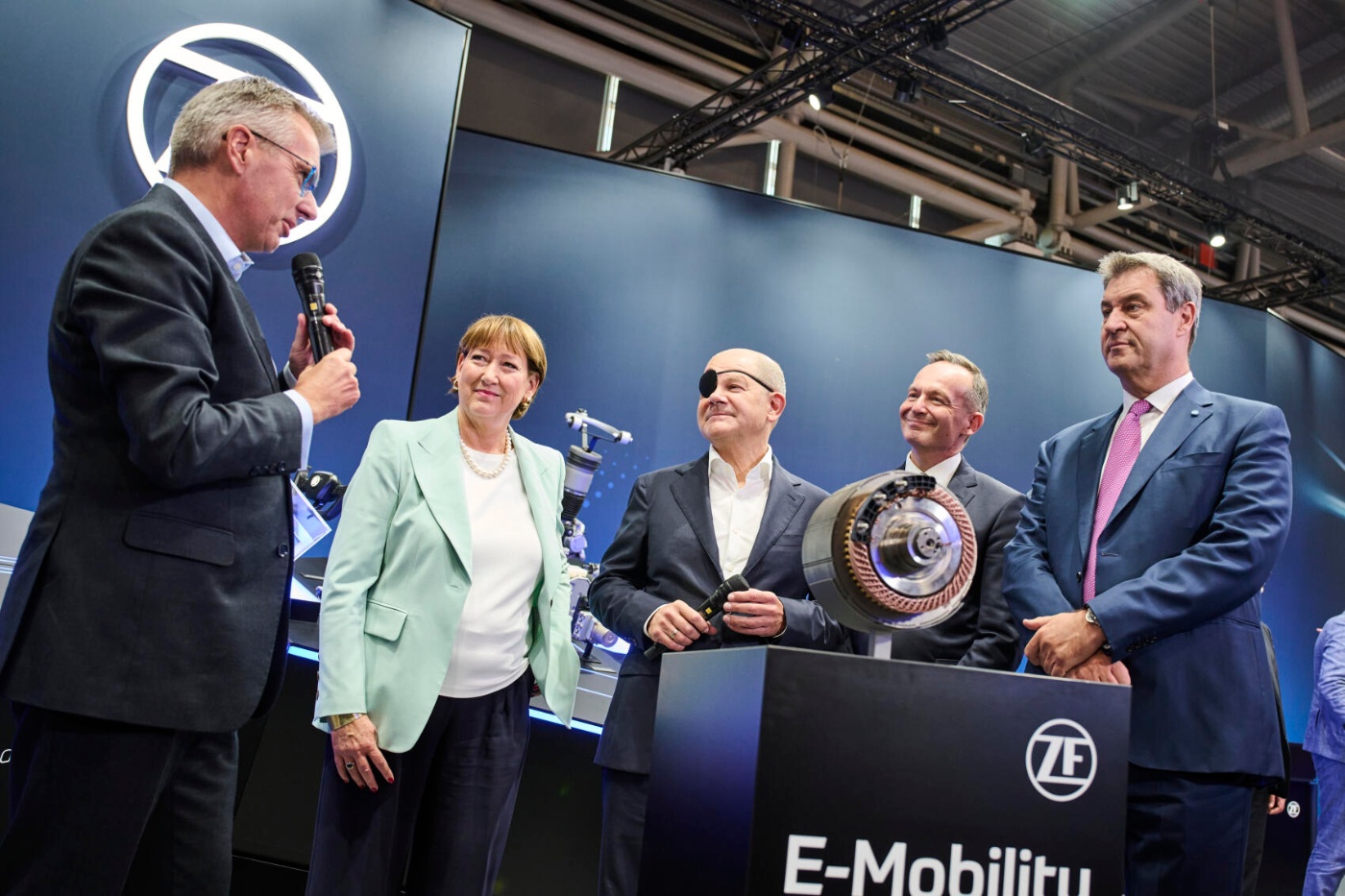 Several people stand at a trade fair booth discussing an e-mobility motor component.