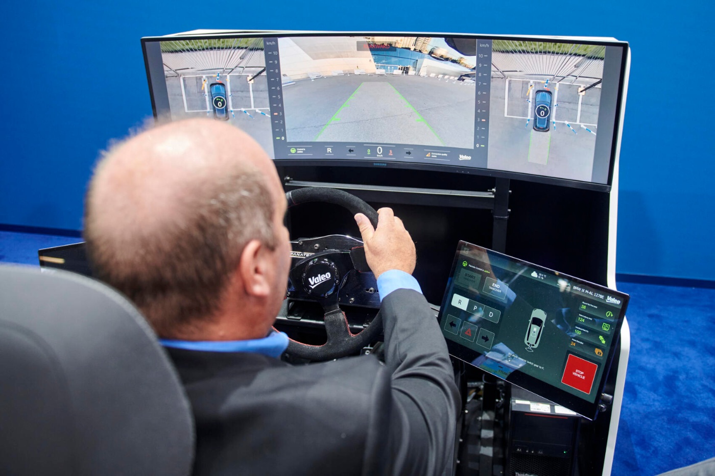 A man tests a driving simulator with multiple screens showing a car’s parking assistance system.