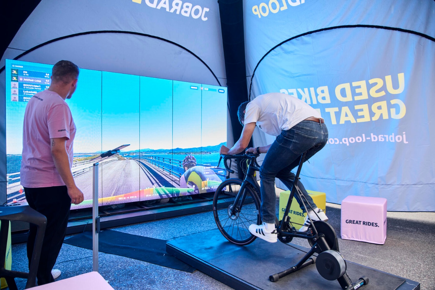 Man rides a stationary racing bike in front of a large virtual cycling screen.