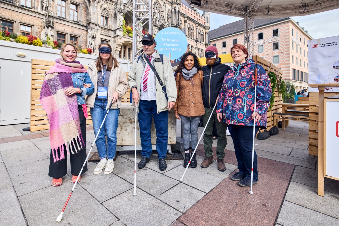 Sechs Personen stehen vor einem Schild zum Inklusionsspaziergang, teils mit Langstöcken und Augenbinden.