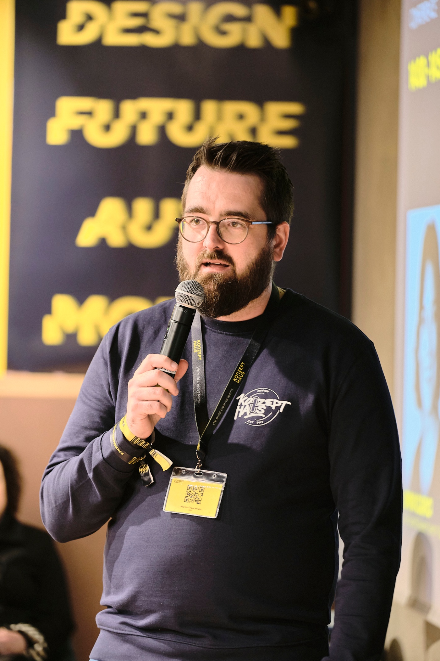 Man with glasses speaks into microphone during a presentation.