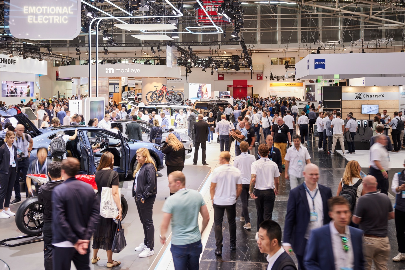 Crowded exhibition hall with electric vehicles, tech booths and people exploring the displays.