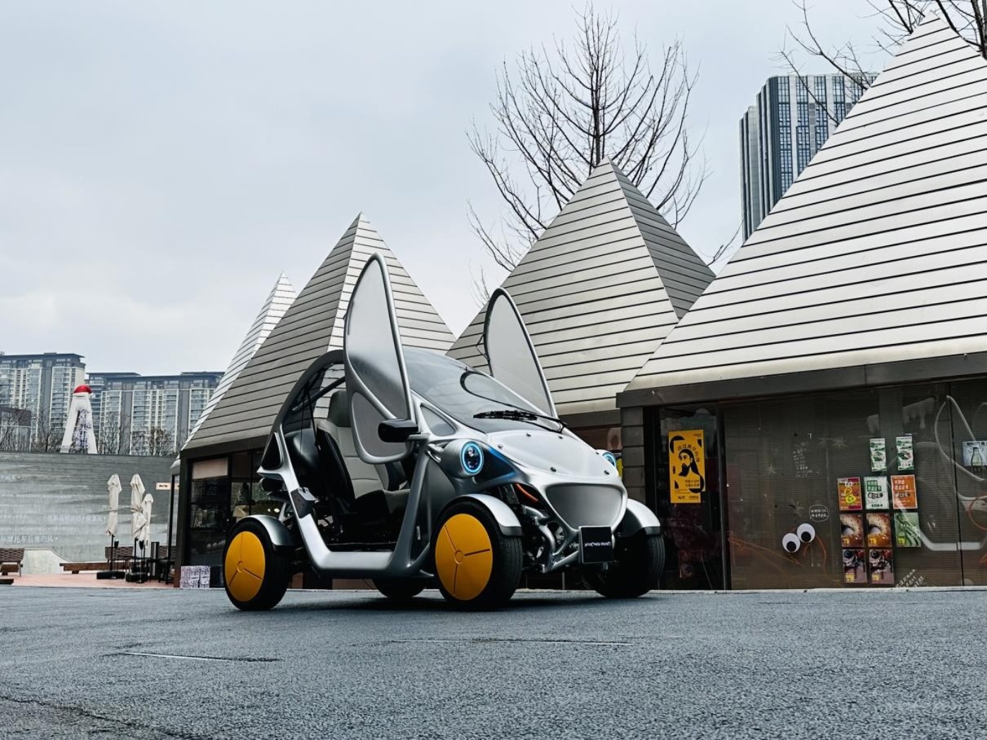 Futuristisches Kompaktauto mit offenen Flügeltüren steht bei modernen, pyramidenförmigen Kiosken.