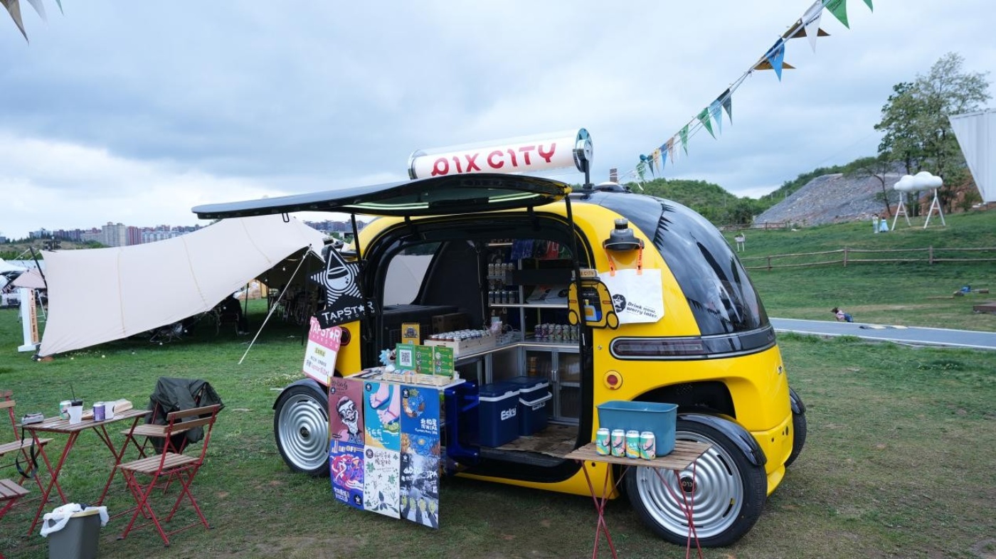 Gelbes autonomes Verkaufsfahrzeug geöffnet und schenkt Getränke auf einem Festival aus.