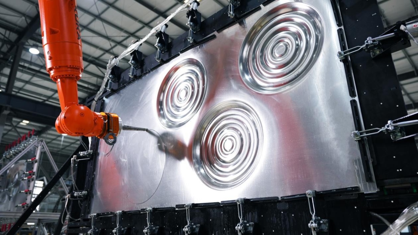 Industrieroboter formt Metallplatte mit kreisförmigen Mustern in einer Fabrikumgebung.