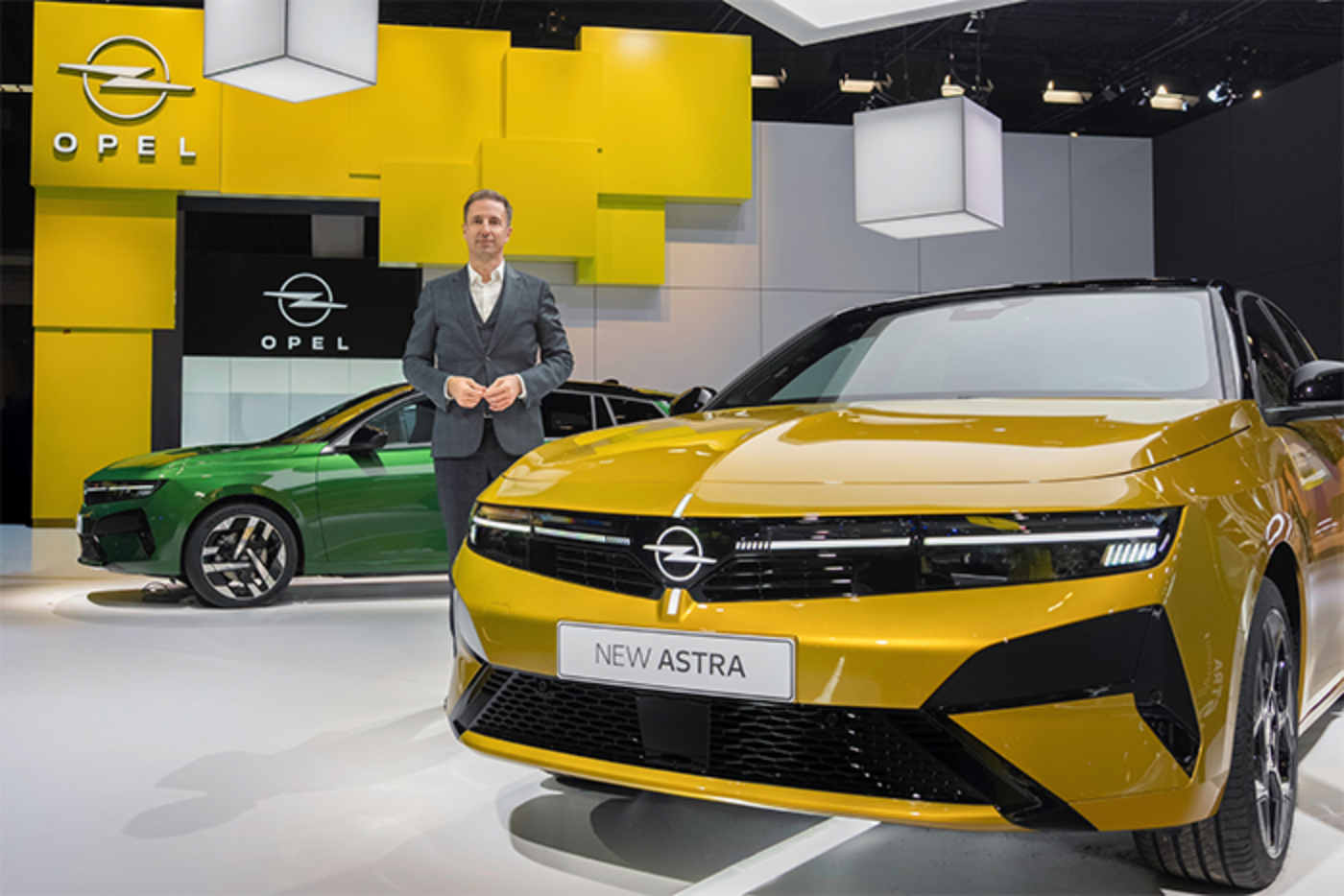 Ein Mann steht an einem Opel-Stand mit gelbem und grünem Astra-Modell im Vordergrund.