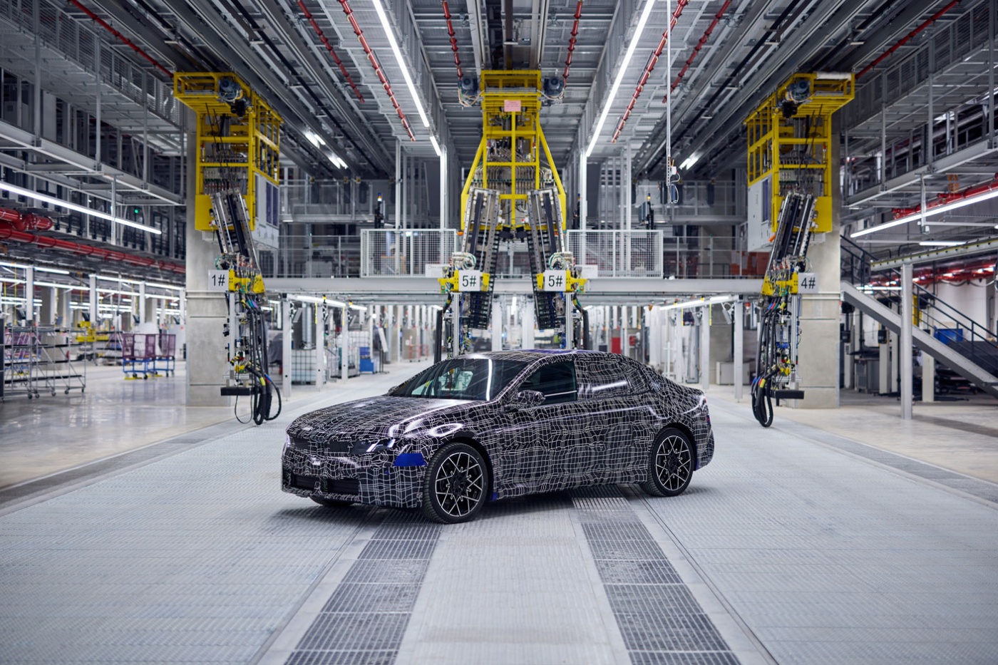 Ein getarntes Testfahrzeug steht in einer modernen, automatisierten Autofabrikhalle.