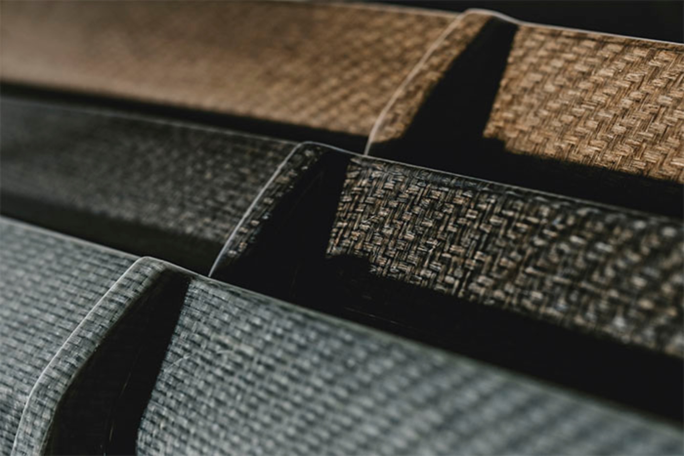 Close-up of stacked woven car interior panels in various dark and natural tones.
