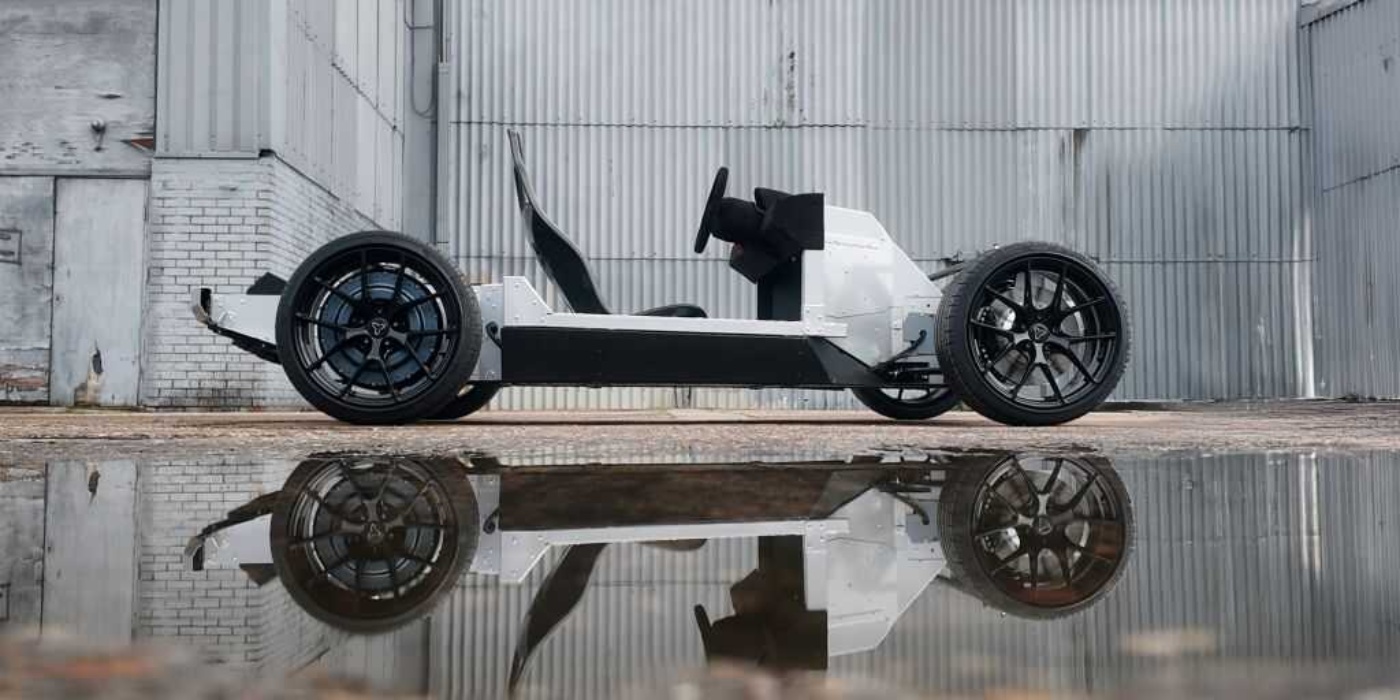 Minimalist electric vehicle chassis with wheels, seat, and steering, reflected in a puddle.