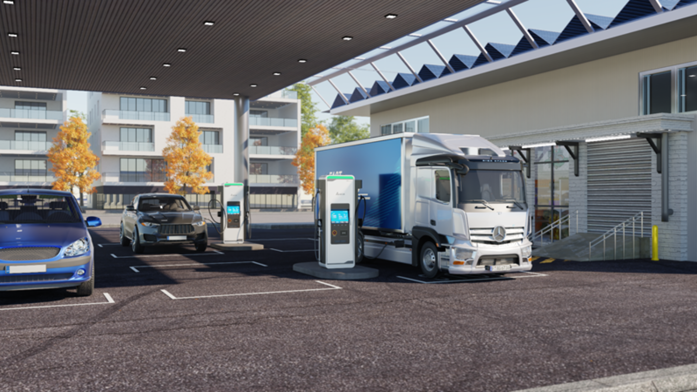 Elektroautos und ein Lkw laden an einer überdachten Ladestation neben einem modernen Gebäude.